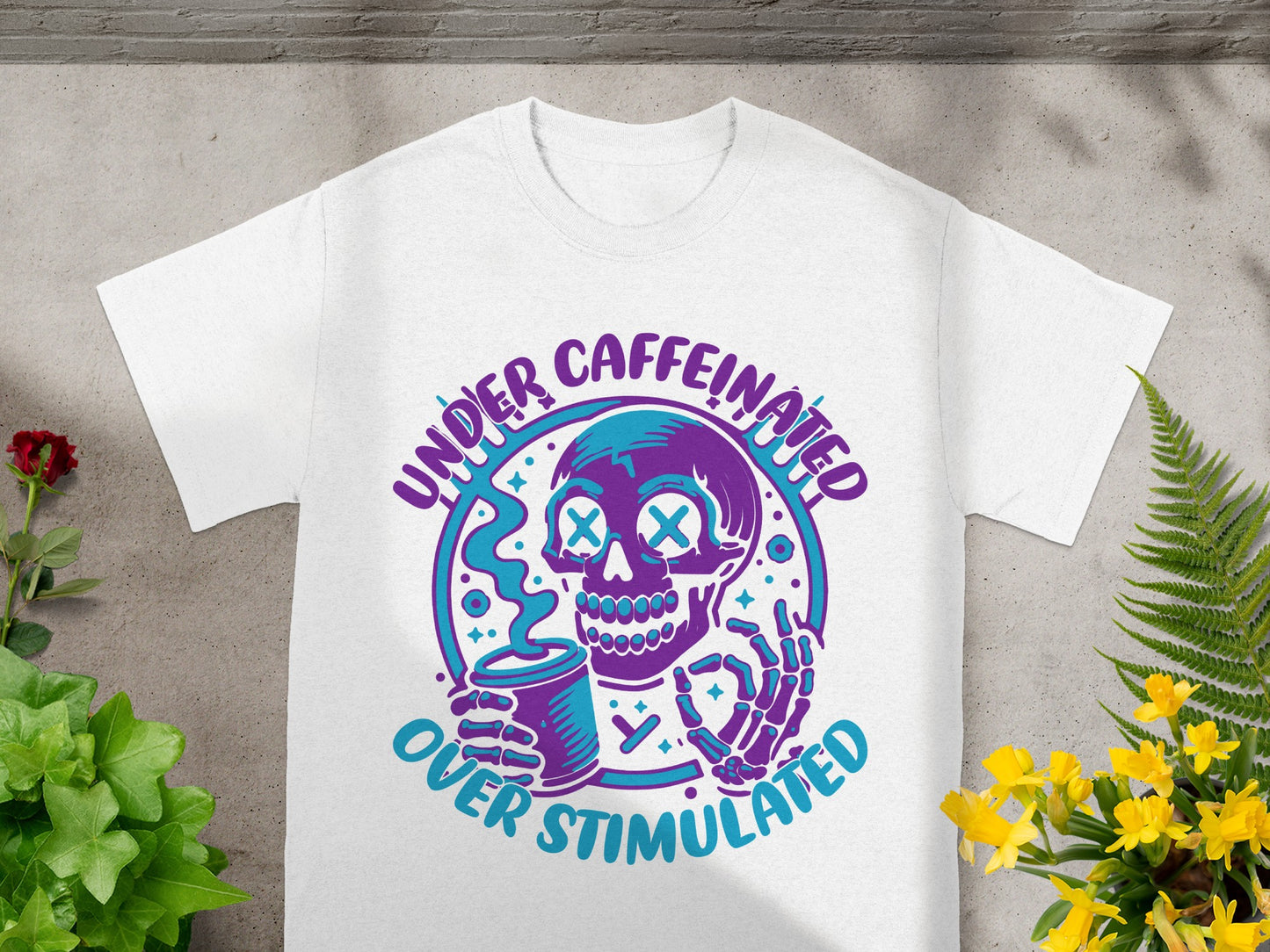 White t-shirt with a purple and teal graphic of a skeleton holding a coffee cup.