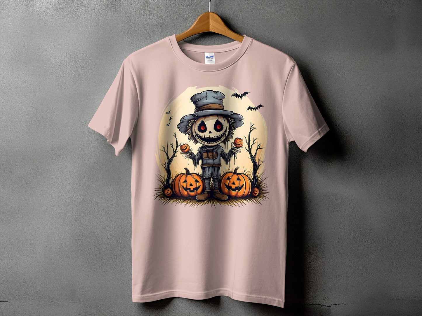 Pink t-shirt with a cartoon scarecrow holding pumpkins and bats, set against a pale moon.