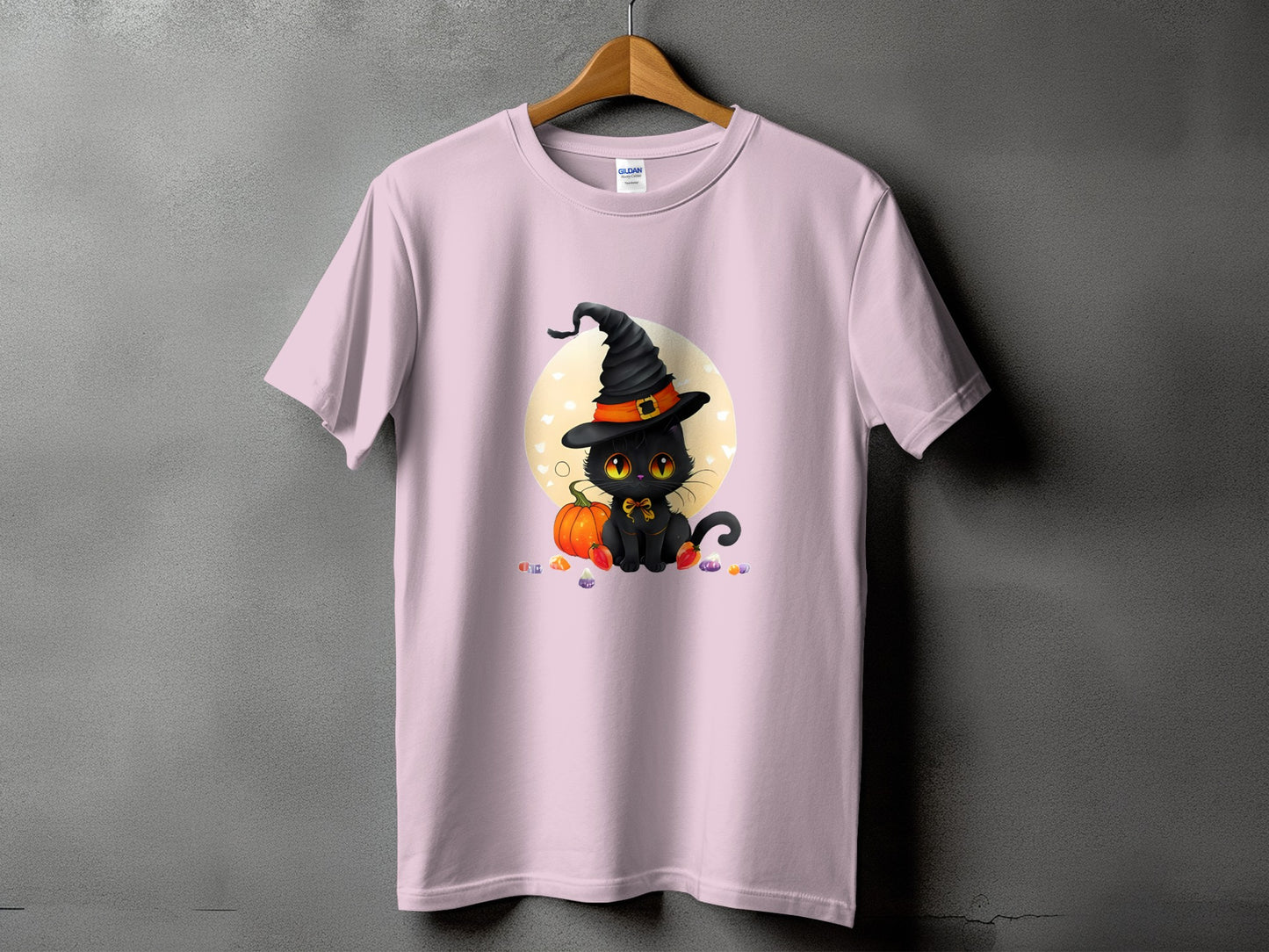 Pink t-shirt with a black cat wearing a witch hat and sitting by a pumpkin.