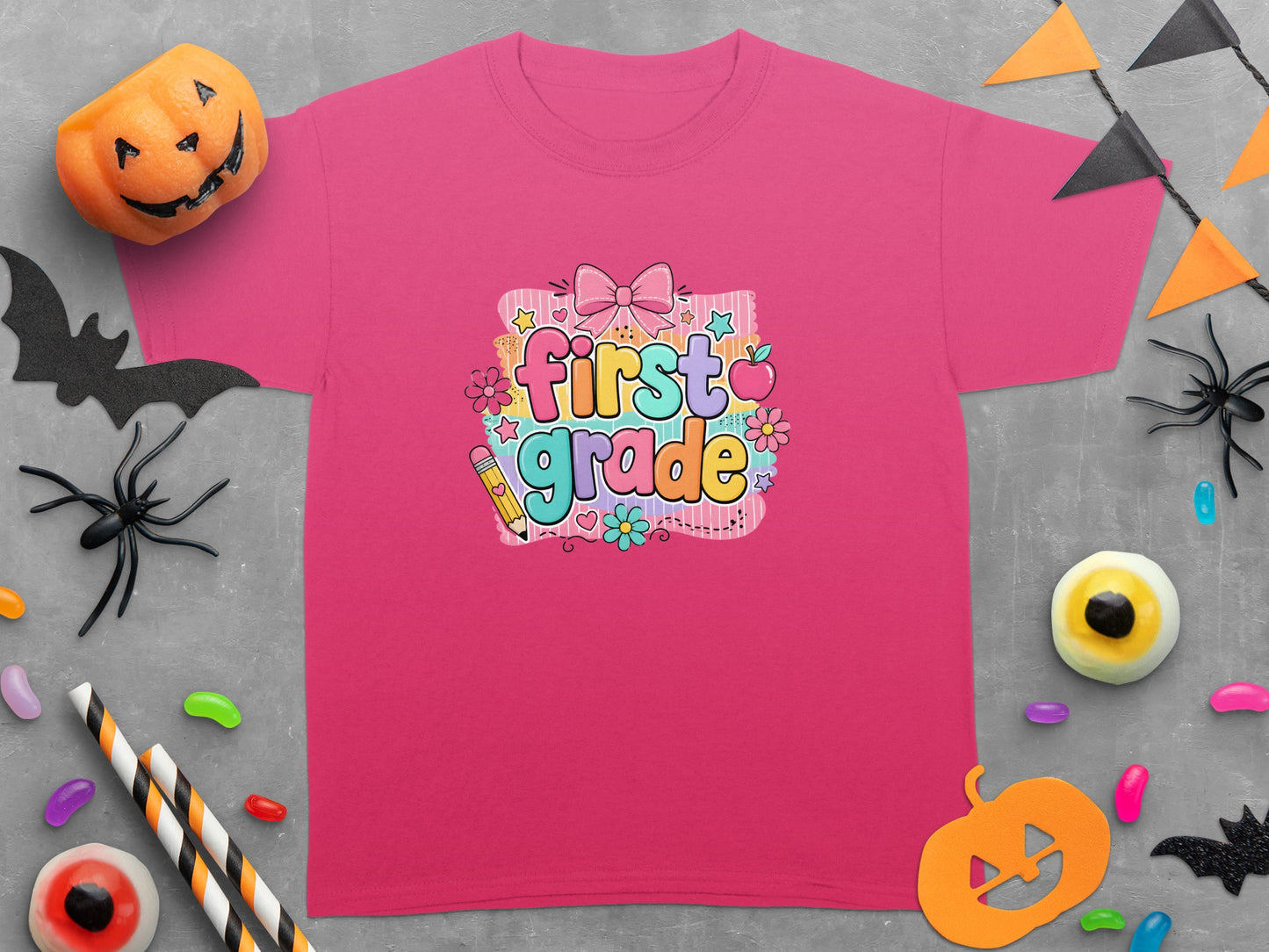 Pink t-shirt with "first grade" graphic featuring colorful letters, bow, apple, and pencil.