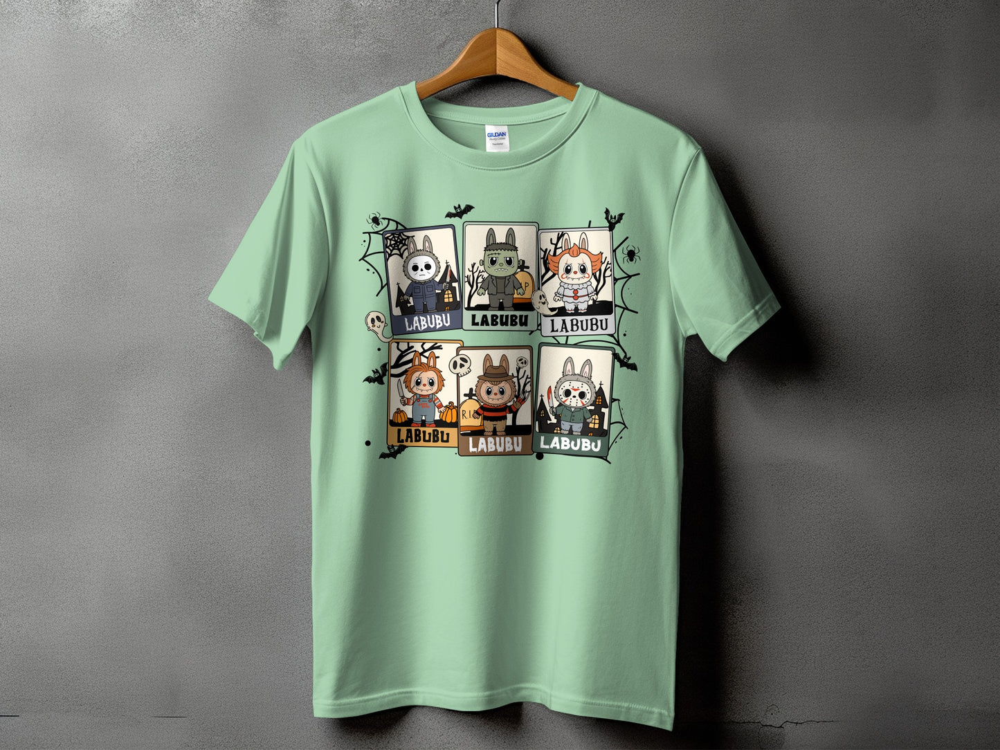 Light green t-shirt with six framed Halloween character illustrations and spiderweb accents.