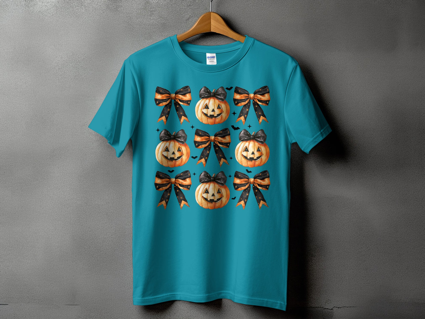Teal t-shirt with a repeating pattern of smiling jack-o'-lanterns and black and orange bows.