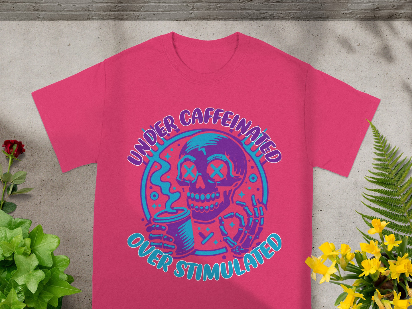 Pink t-shirt with skull graphic and text "UNDER CAFFEINATED OVER STIMULATED."