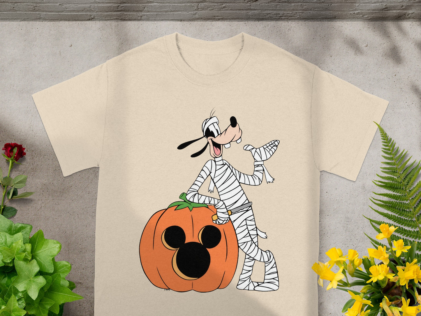 Goofy as a mummy leaning on a Mickey Mouse jack-o'-lantern.