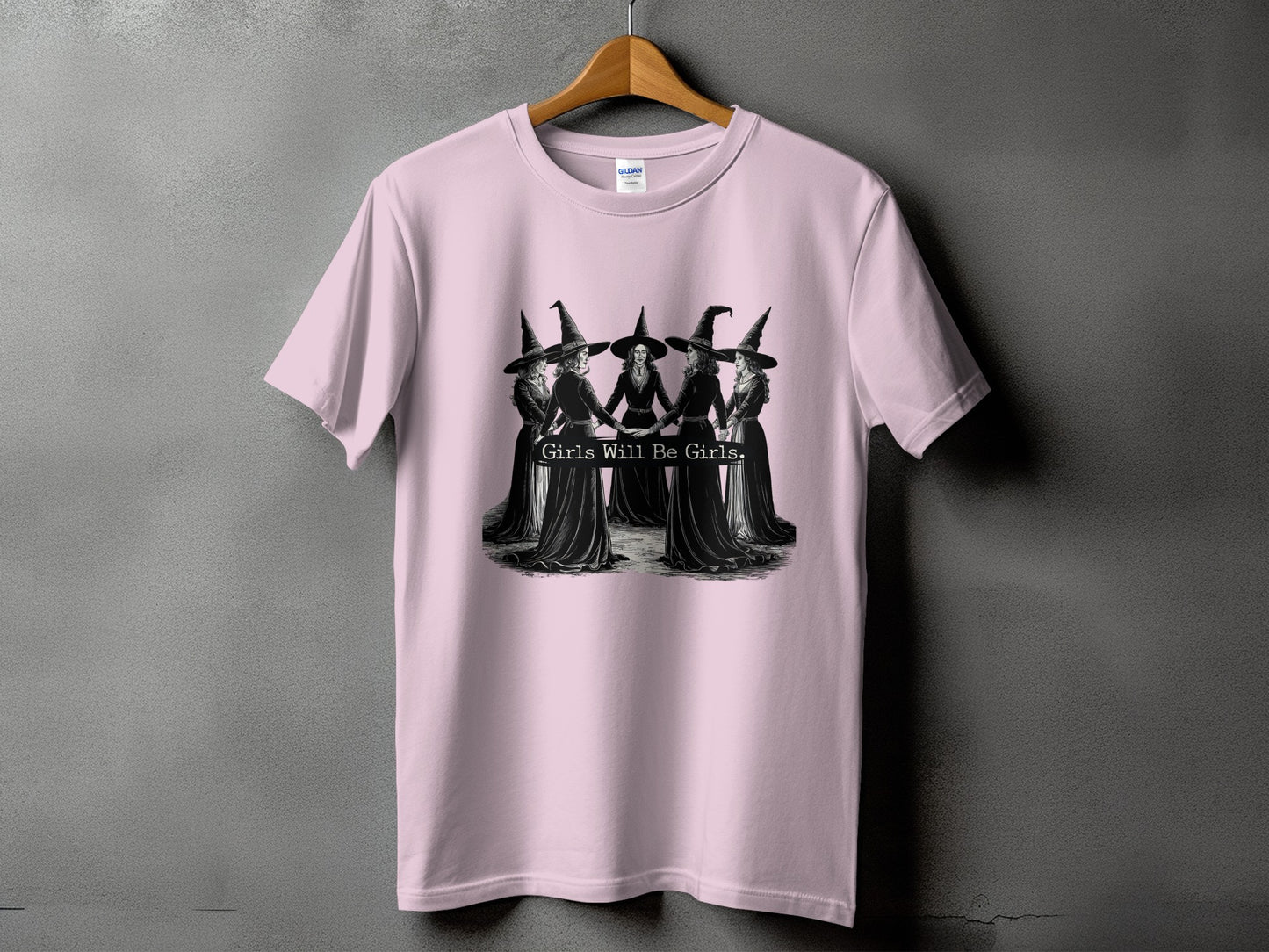 Pink t-shirt with five witches in a circle, text "Girls Will Be Girls."
