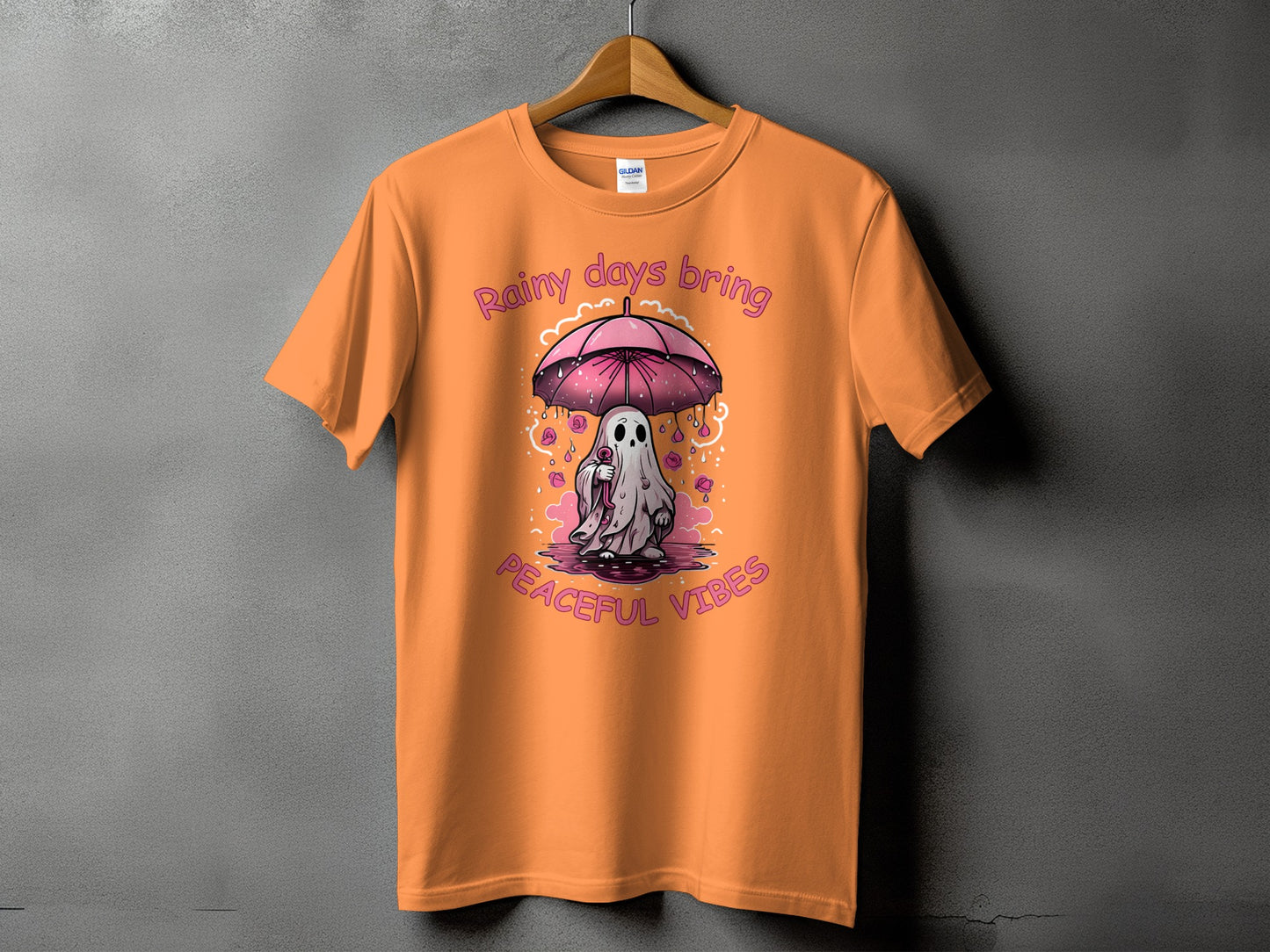 Orange t-shirt with a ghost under a pink umbrella and the text "Rainy days bring peaceful vibes."