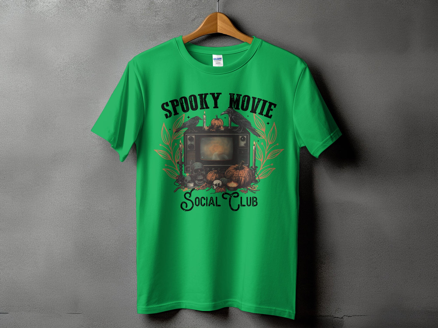 Green t-shirt with "Spooky Movie Social Club" Halloween graphic featuring a TV, skulls, and pumpkins.