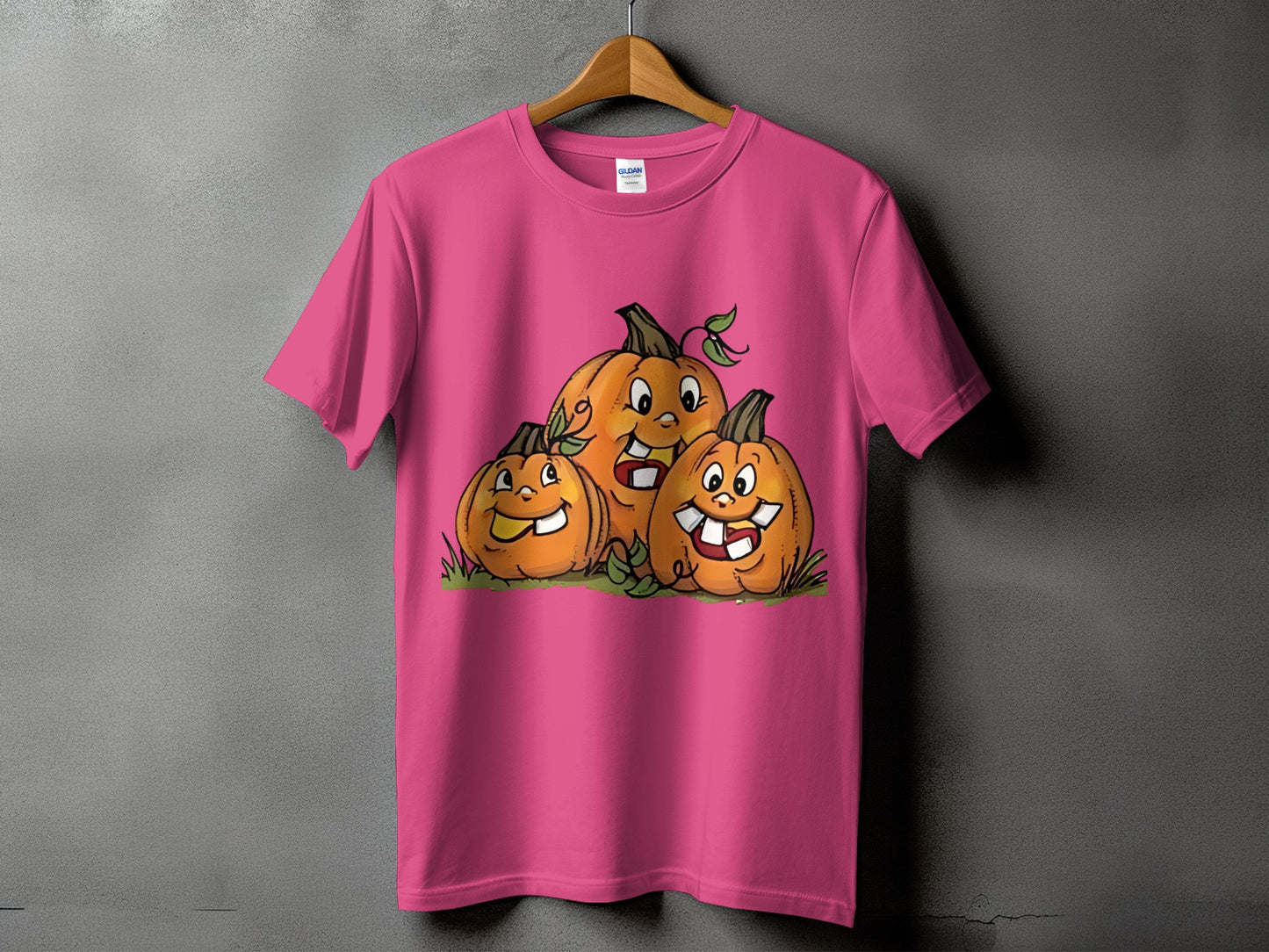 Pink t-shirt with three cartoon pumpkins smiling on a gray background.