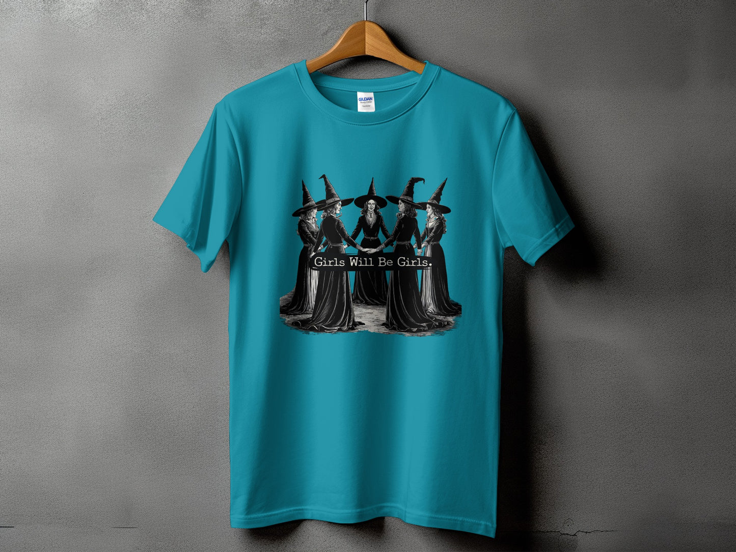 Teal t-shirt with black and white graphic of witches holding hands, reading "Girls Will Be Girls."