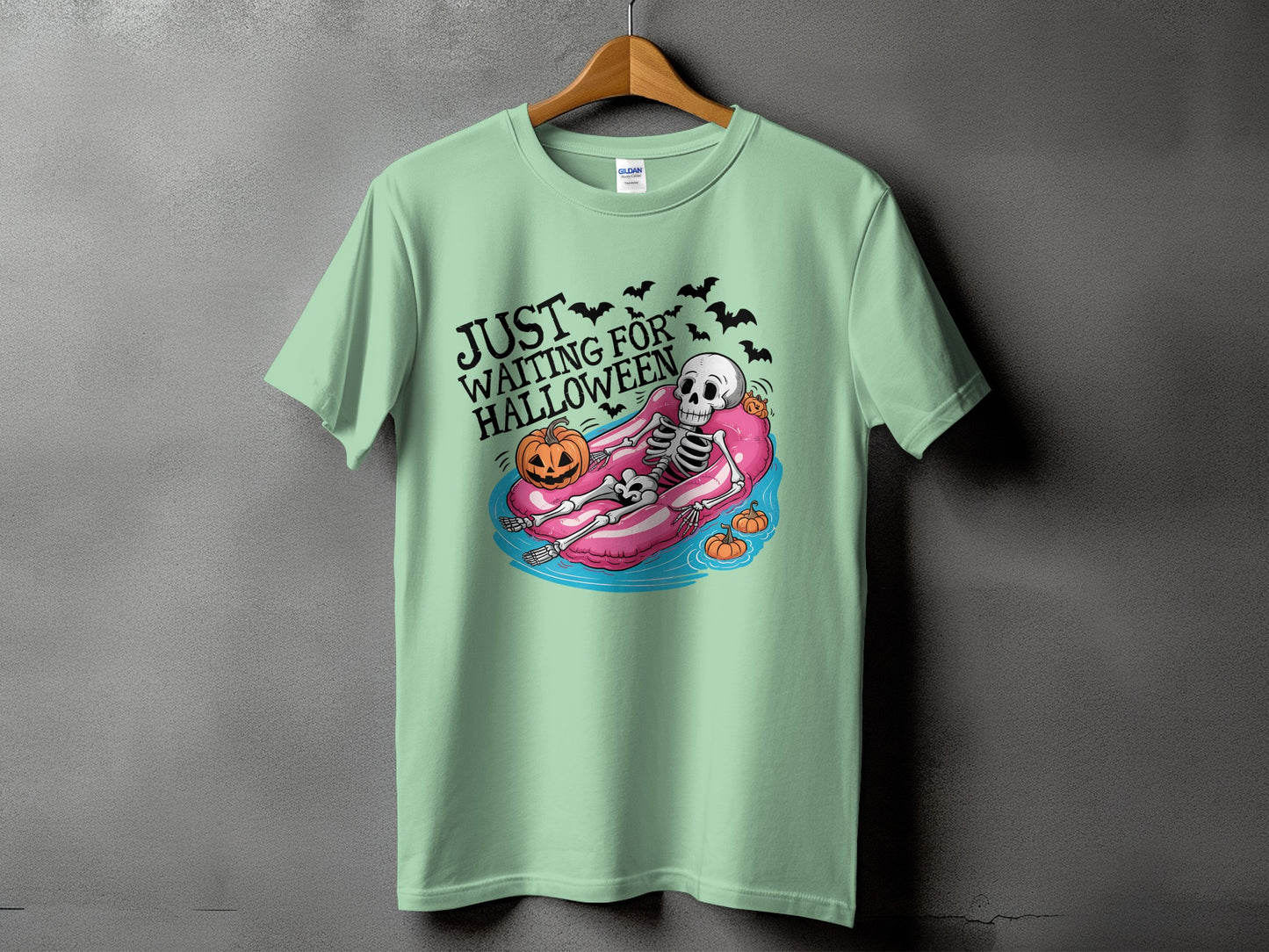 Green t-shirt with skeleton on inflatable tube and text "JUST WAITING FOR HALLOWEEN".