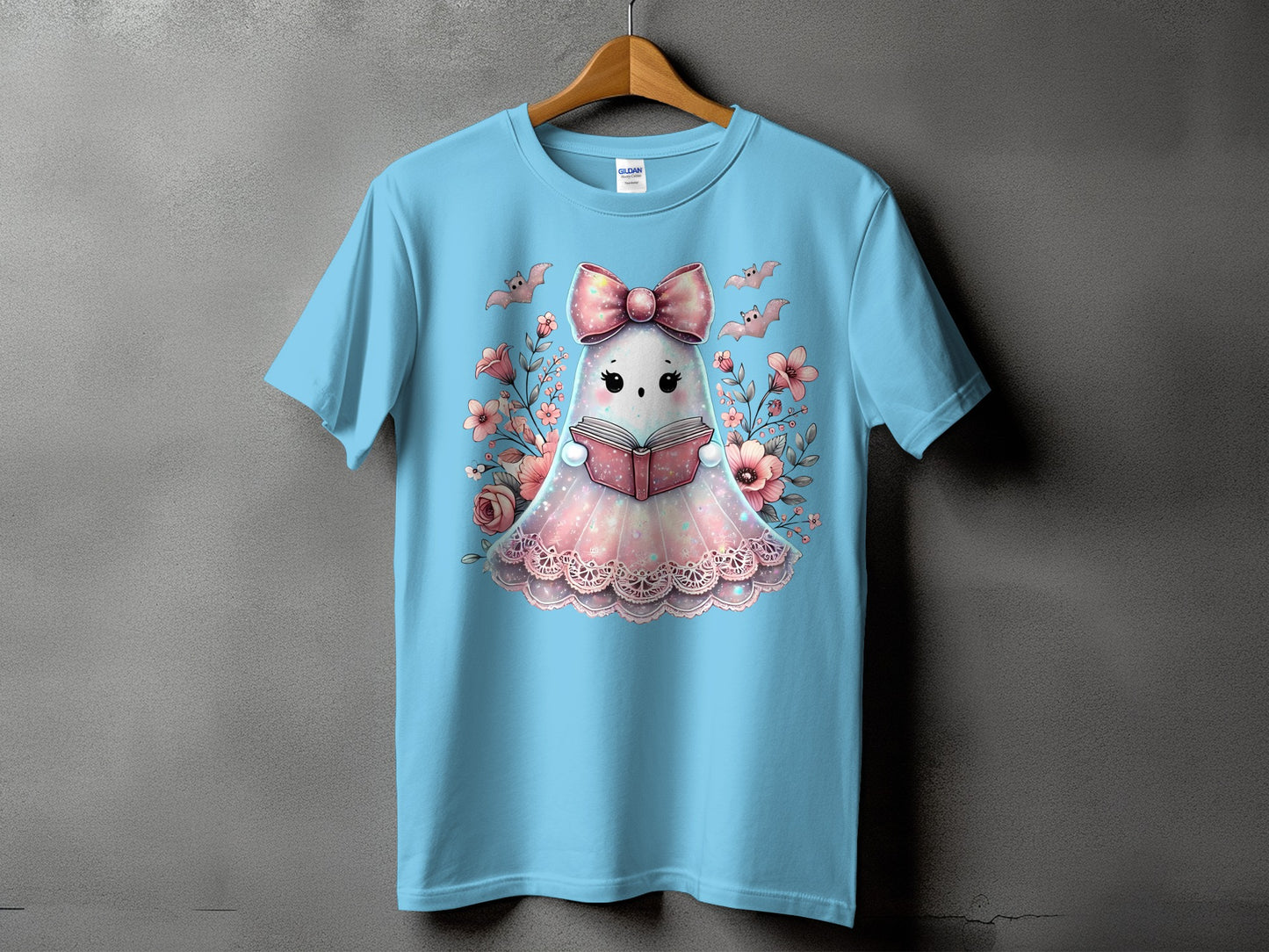 Light blue t-shirt with a cute ghost reading a book surrounded by flowers and bats.