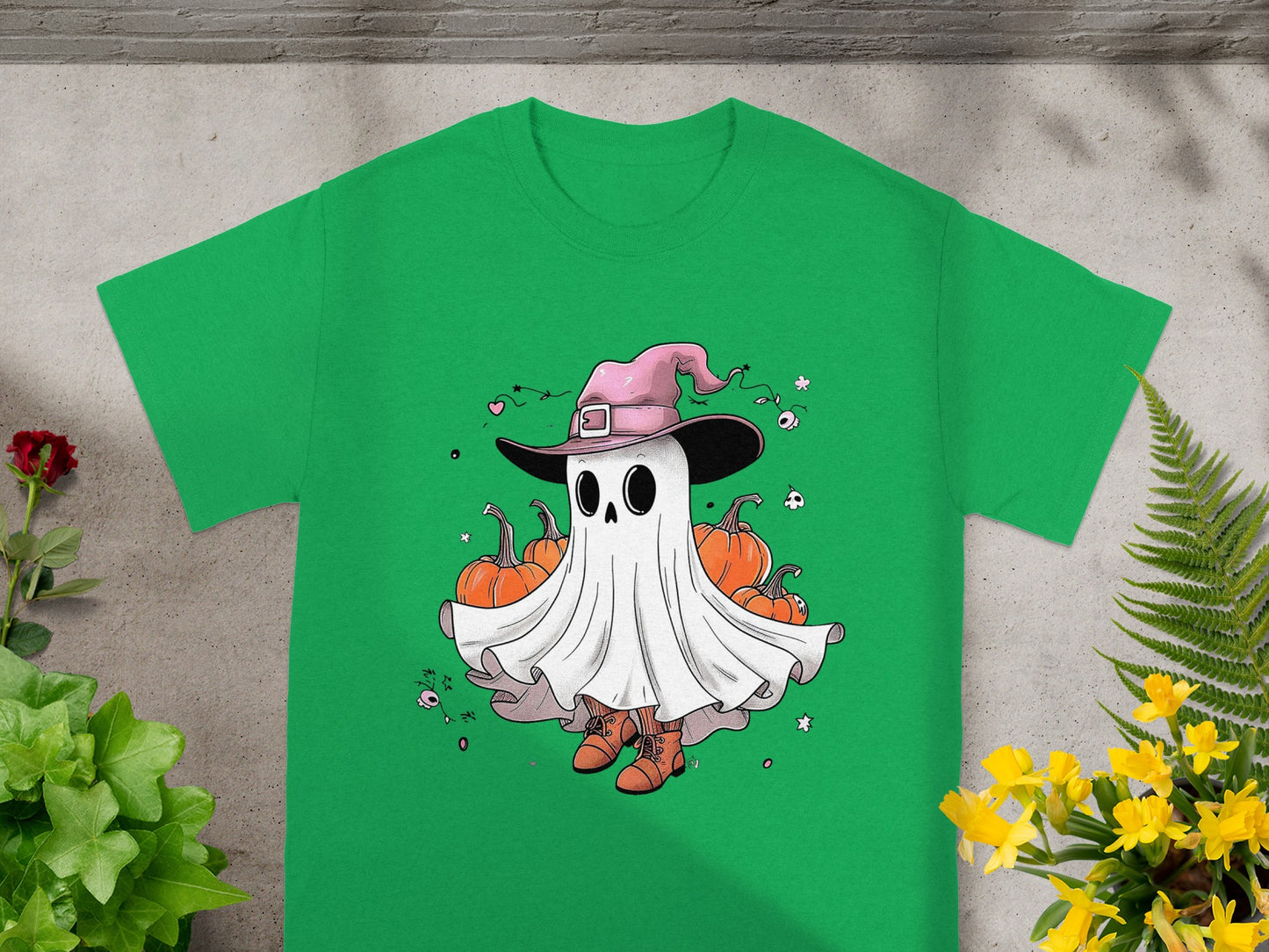 Green t-shirt with a cartoon ghost wearing a pink witch hat, surrounded by pumpkins.