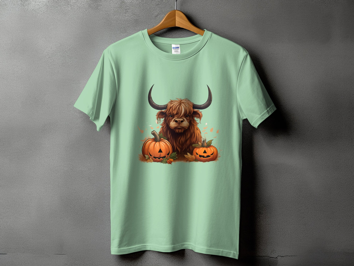 Highland cow with pumpkins and autumn leaves graphic on light green t-shirt.