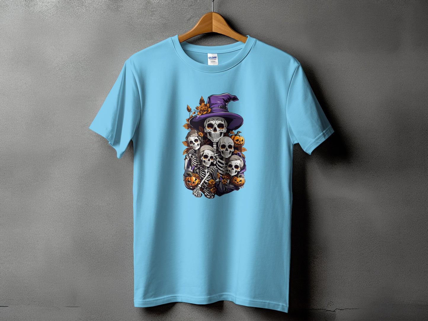 Light blue t-shirt with a Halloween graphic of skeletons wearing a witch hat and pumpkins.