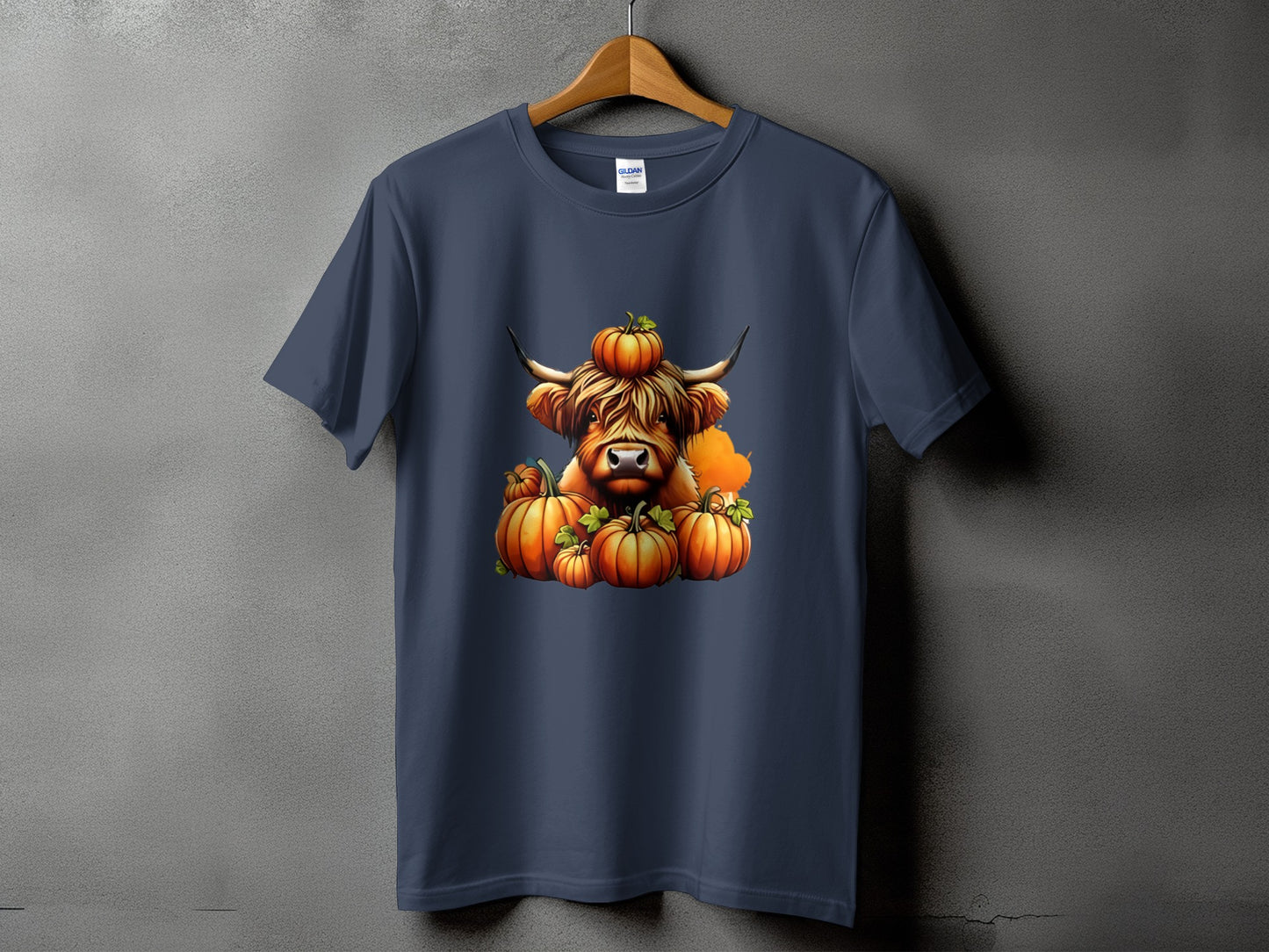 Navy t-shirt with a Highland cow wearing a pumpkin on its head surrounded by pumpkins.