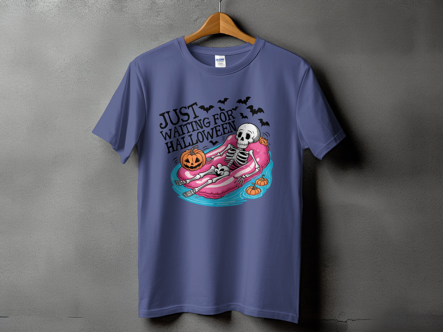 Skeleton floating on pink tube with pumpkins and bats, text "JUST WAITING FOR HALLOWEEN".