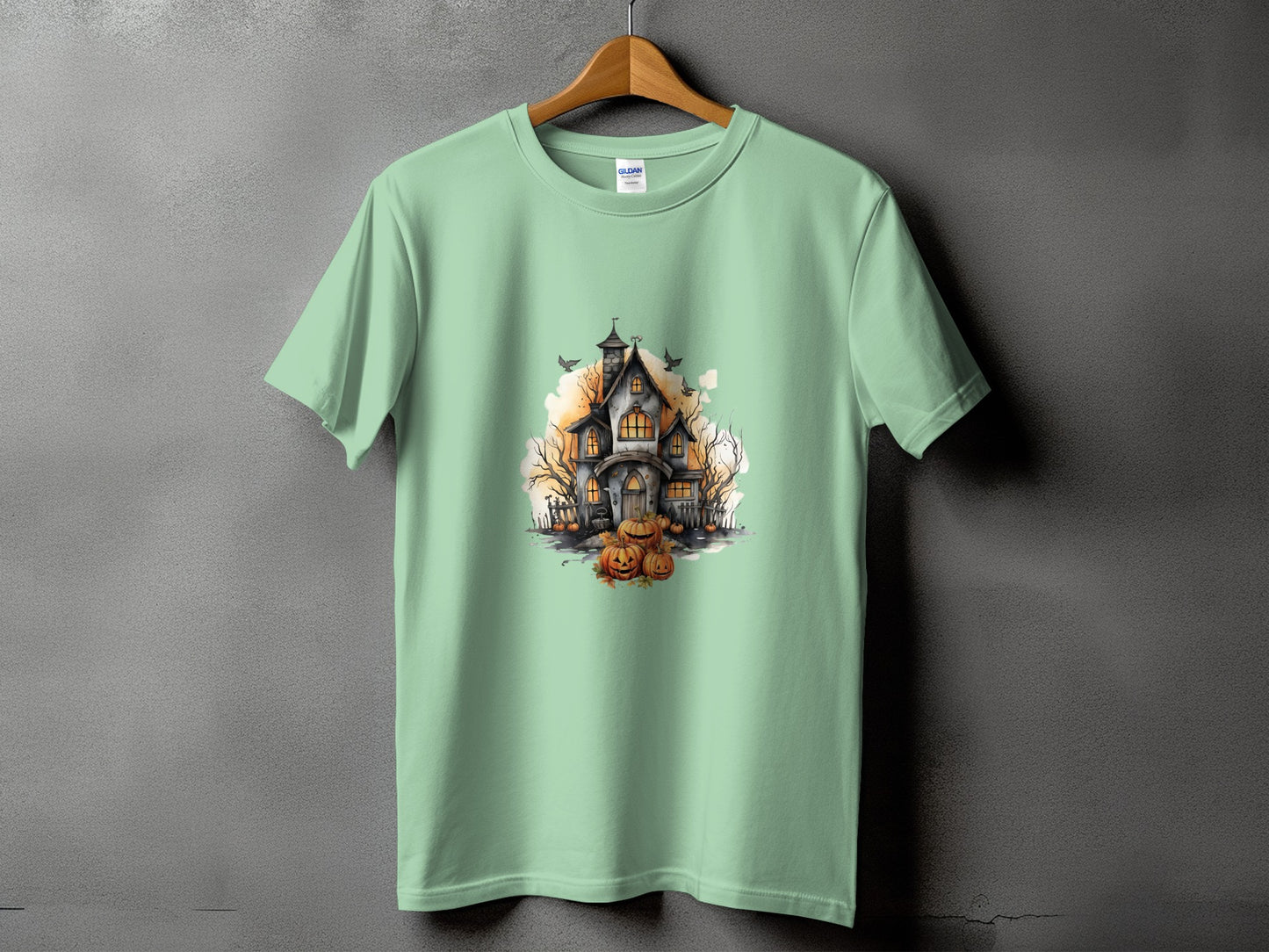 Light green t-shirt with a watercolor illustration of a haunted house and pumpkins.