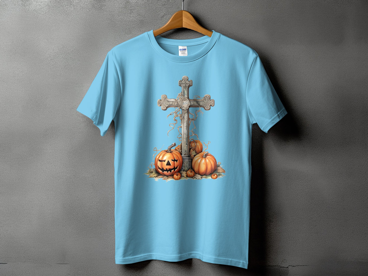 Light blue t-shirt with a gray cross, carved pumpkins, and autumn leaves graphic.