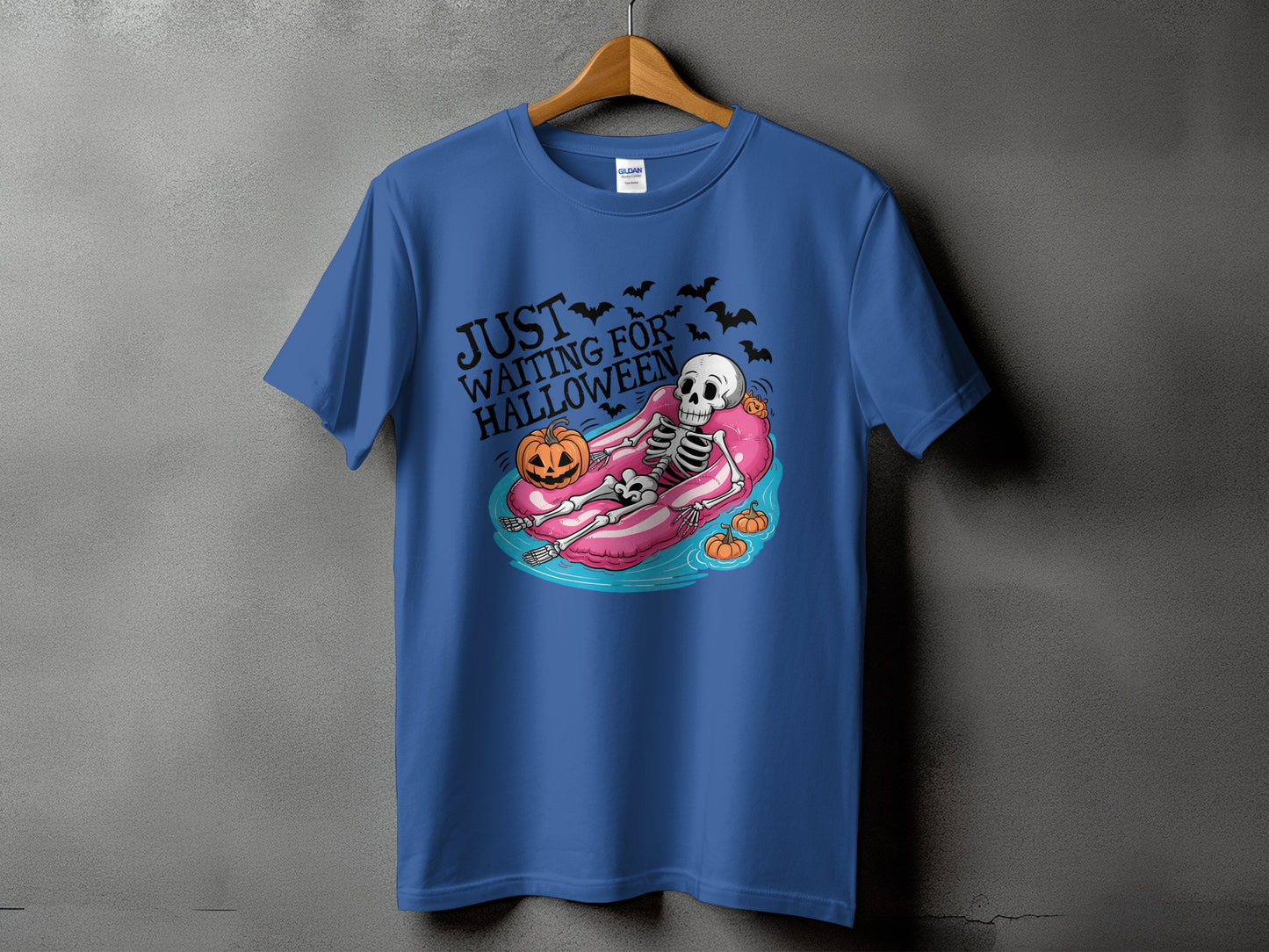Blue t-shirt with skeleton on pink float, text "Just Waiting For Halloween," pumpkins, bats.