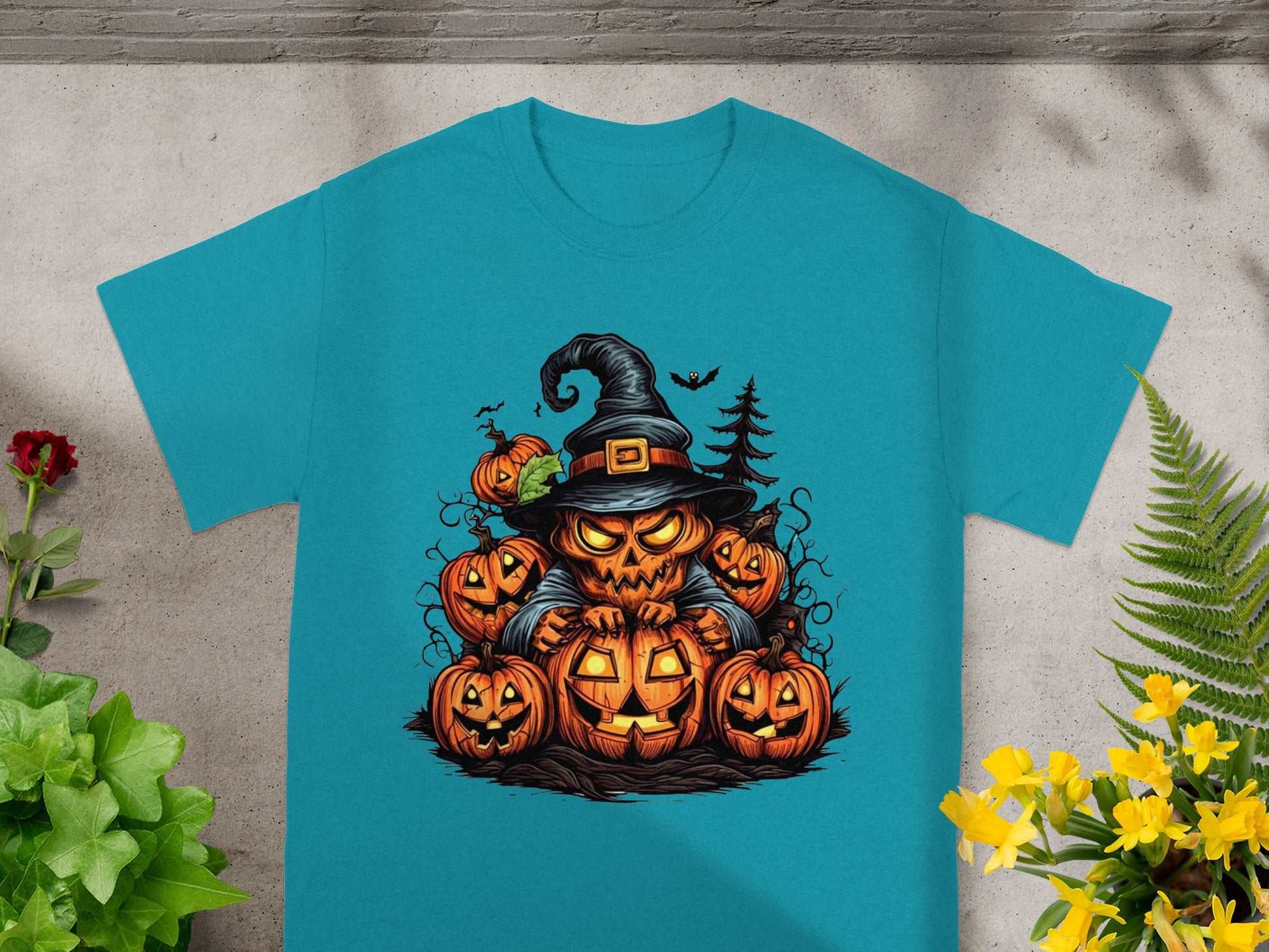 Jack-o'-lantern witch surrounded by pumpkins and bats on a teal t-shirt.