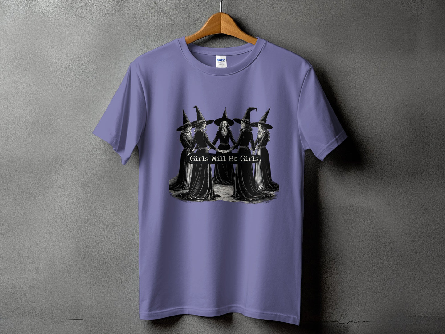 Purple t-shirt with a circular design of witches holding hands and text "Girls Will Be Girls."