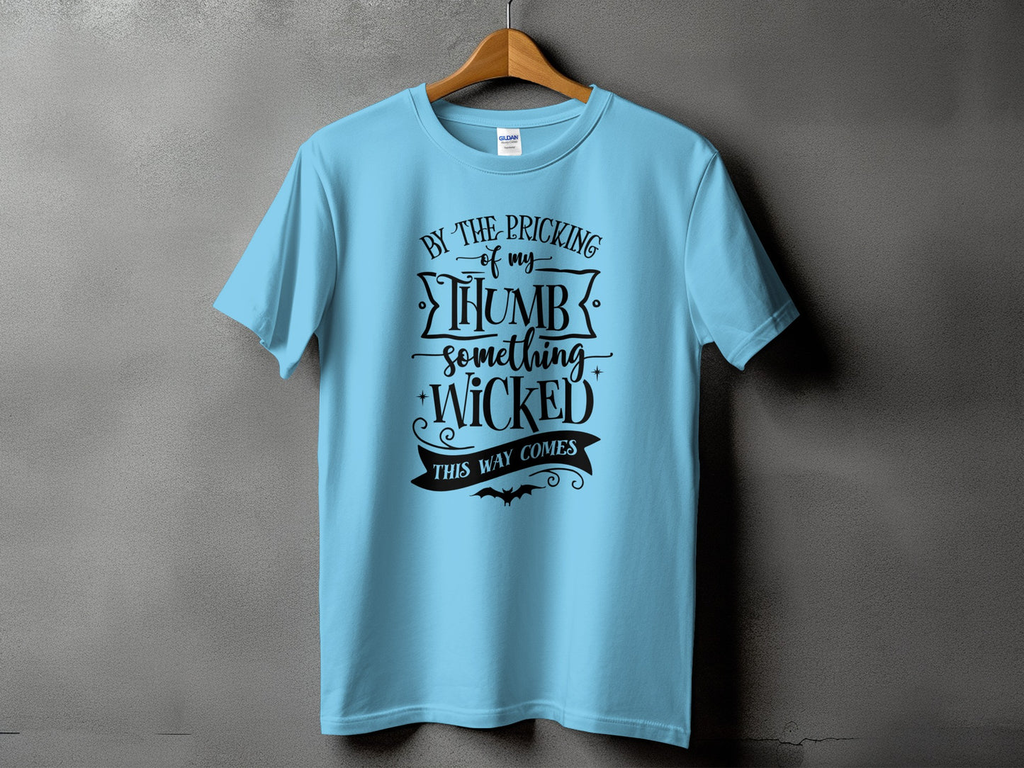 Light blue t-shirt with black text "By the pricking of my thumb, something wicked this way comes."