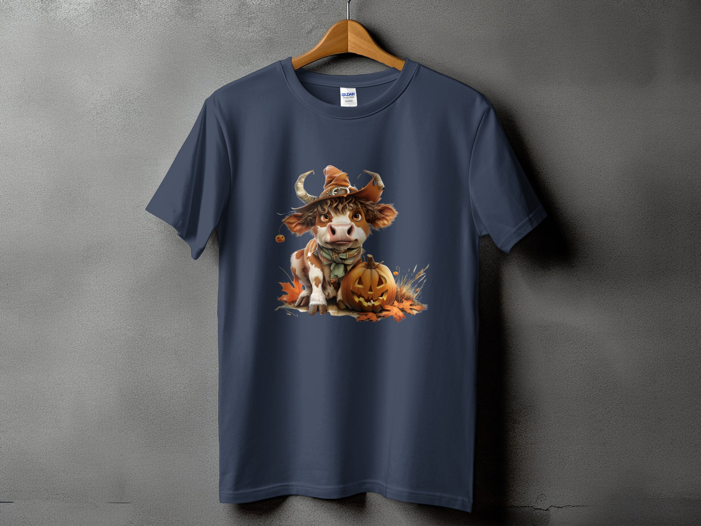 T-shirt with a Halloween cow wearing a witch hat and scarf, next to a jack-o'-lantern.