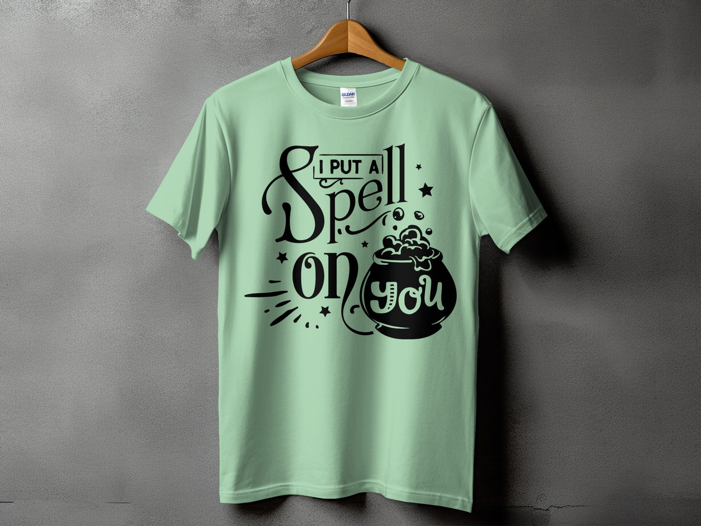 Light green t-shirt with black text and cauldron graphic saying "I put a spell on you."