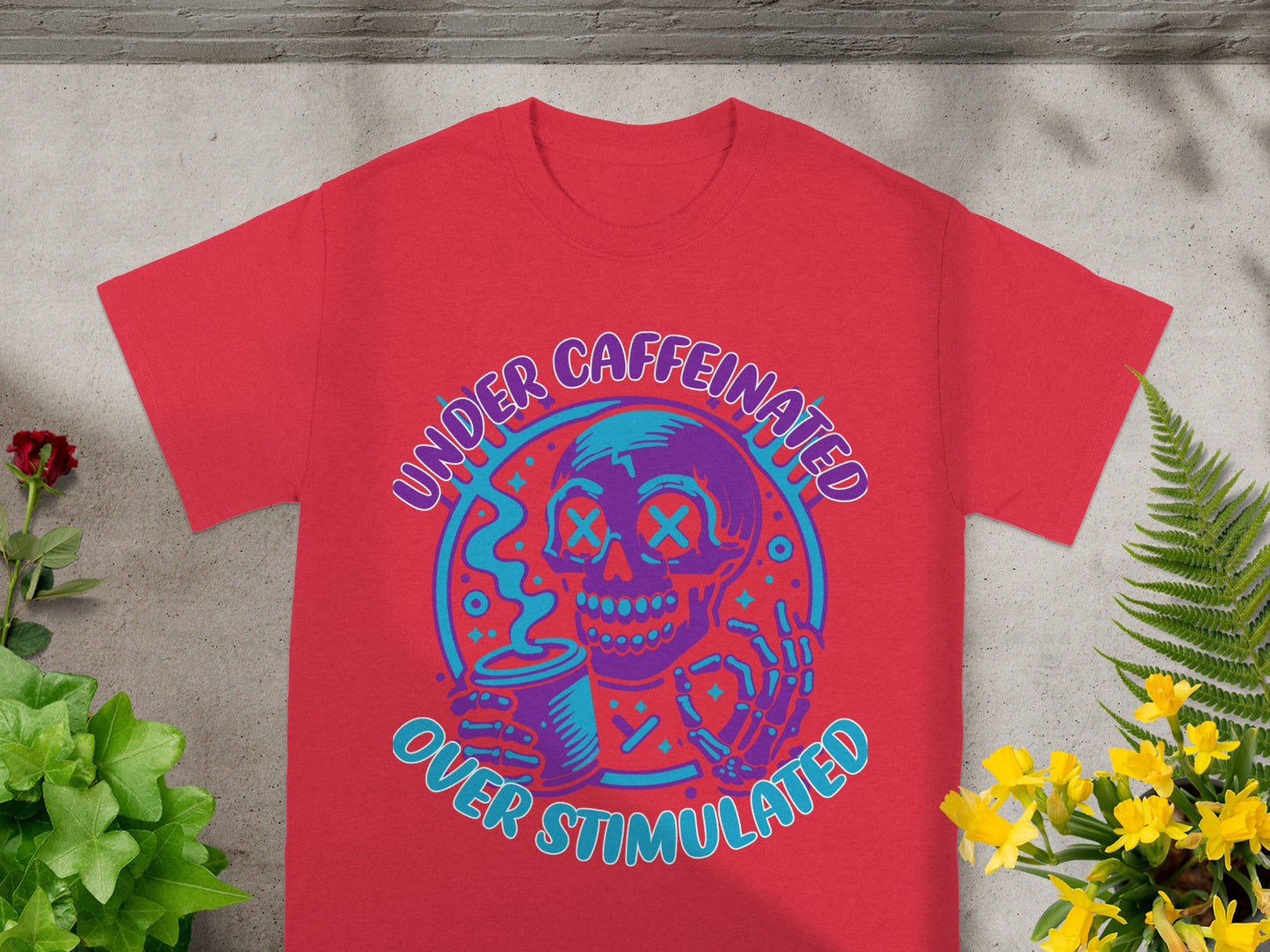 Red t-shirt with a graphic of a skull holding a coffee cup and text "UNDER CAFFEINATED OVER STIMULATED."