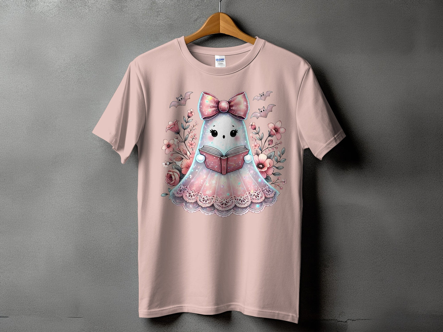 Pink t-shirt with a cute ghost character reading a book, surrounded by flowers and bats.