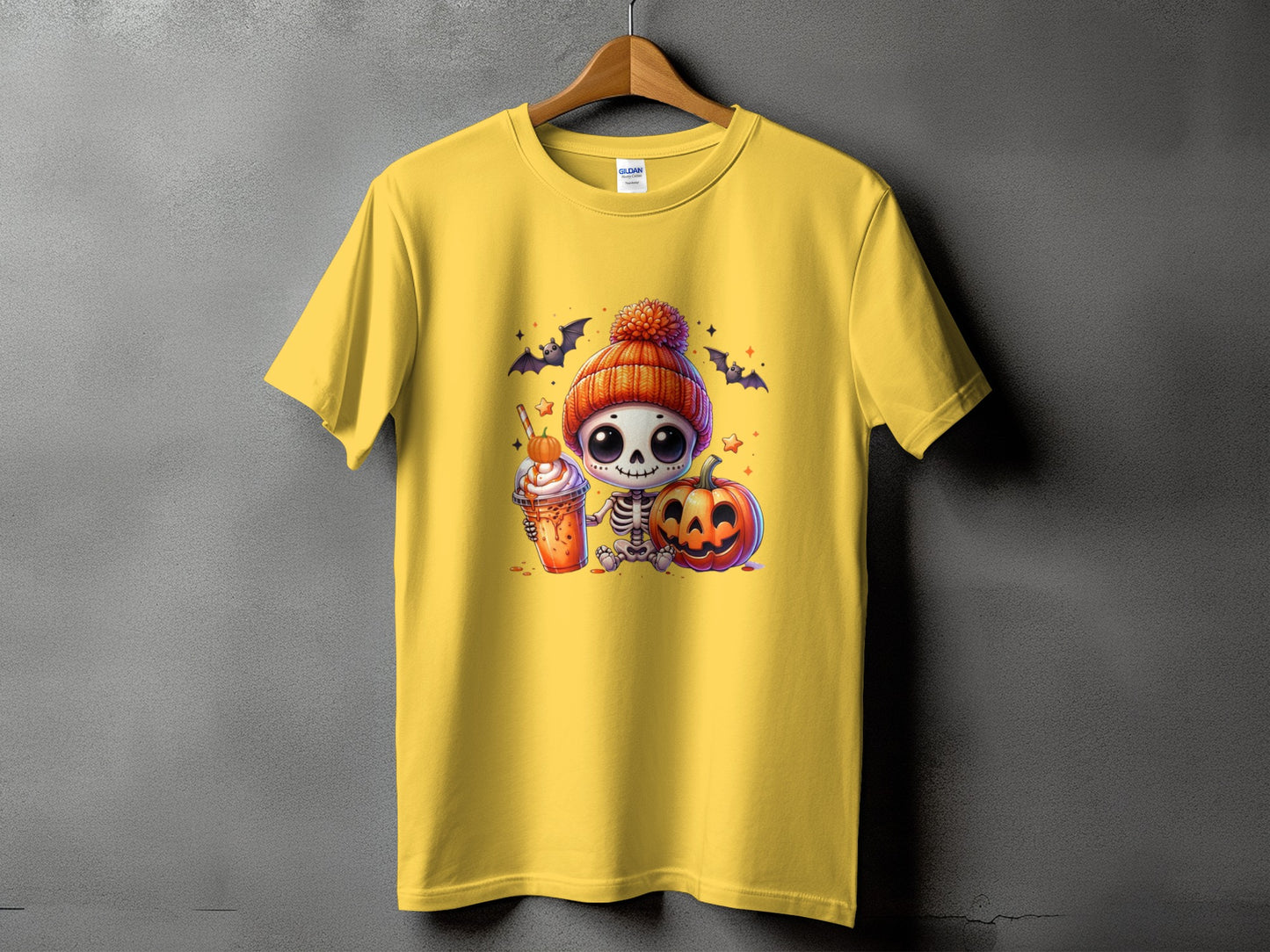 Yellow t-shirt with a cartoon skeleton holding a pumpkin spice drink and sitting by a jack-o'-lantern.