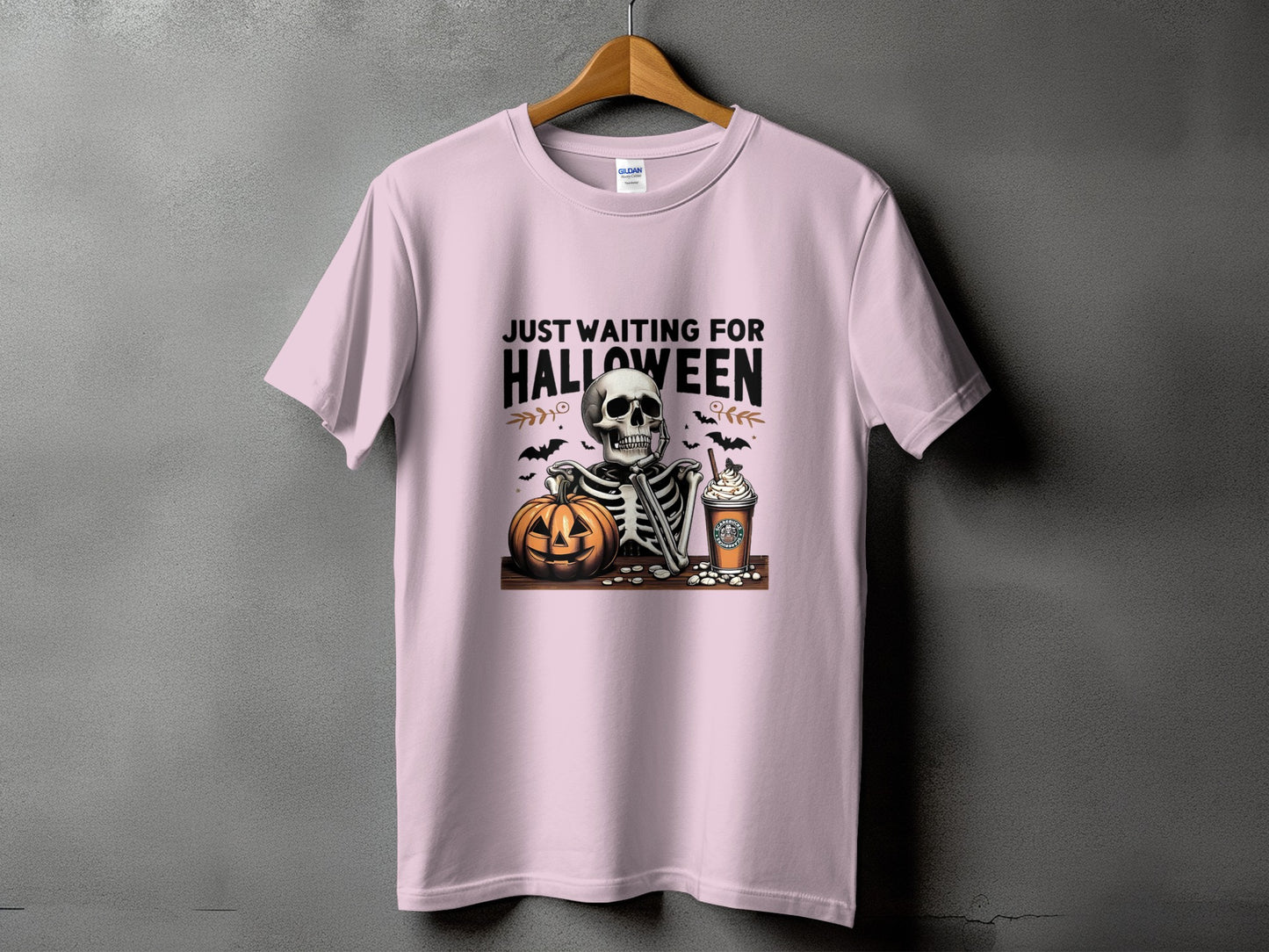 Pink t-shirt with skeleton, pumpkin, coffee, and bats graphic that says "Just Waiting For Halloween".