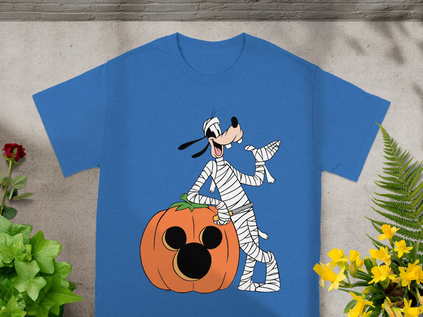 Goofy dressed as a mummy poses with a Mickey Mouse pumpkin on a blue t-shirt.