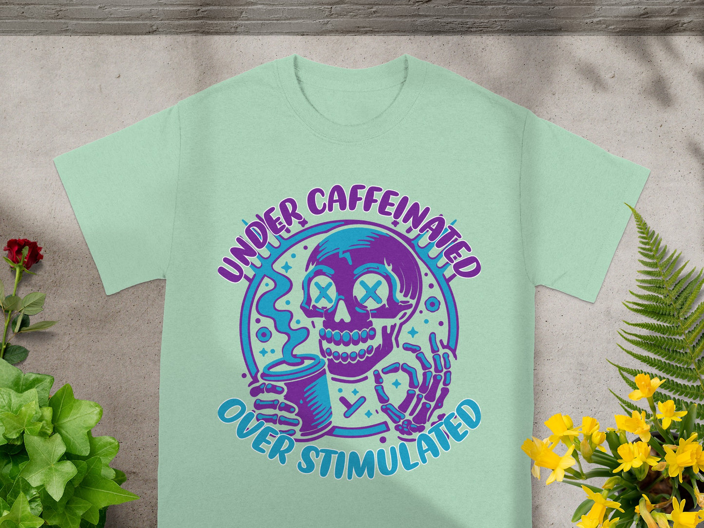 Mint t-shirt with skull graphic and text reading "UNDER CAFFEINATED OVER STIMULATED."