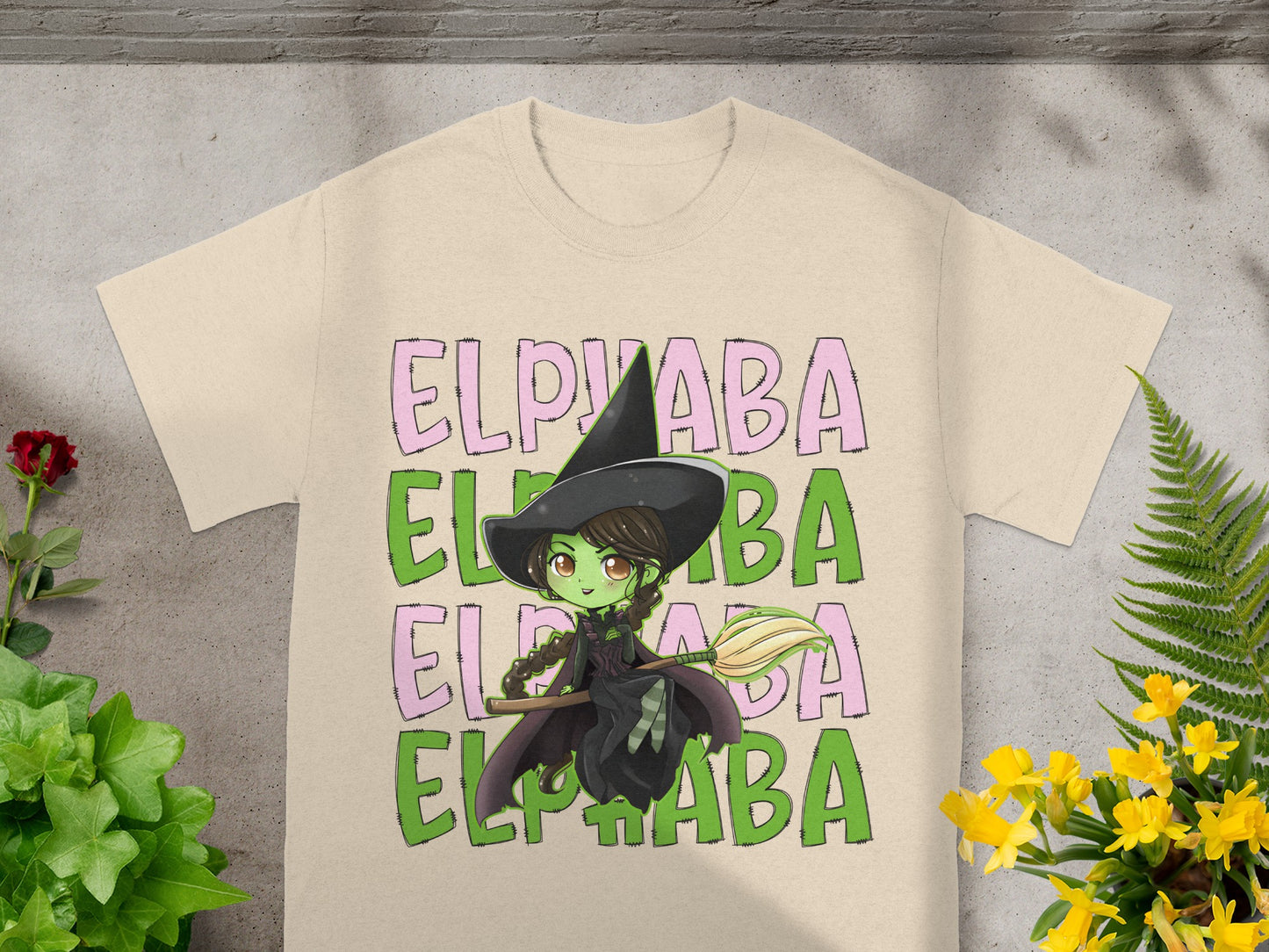 Elphaba witch graphic with broom on a cream t-shirt.