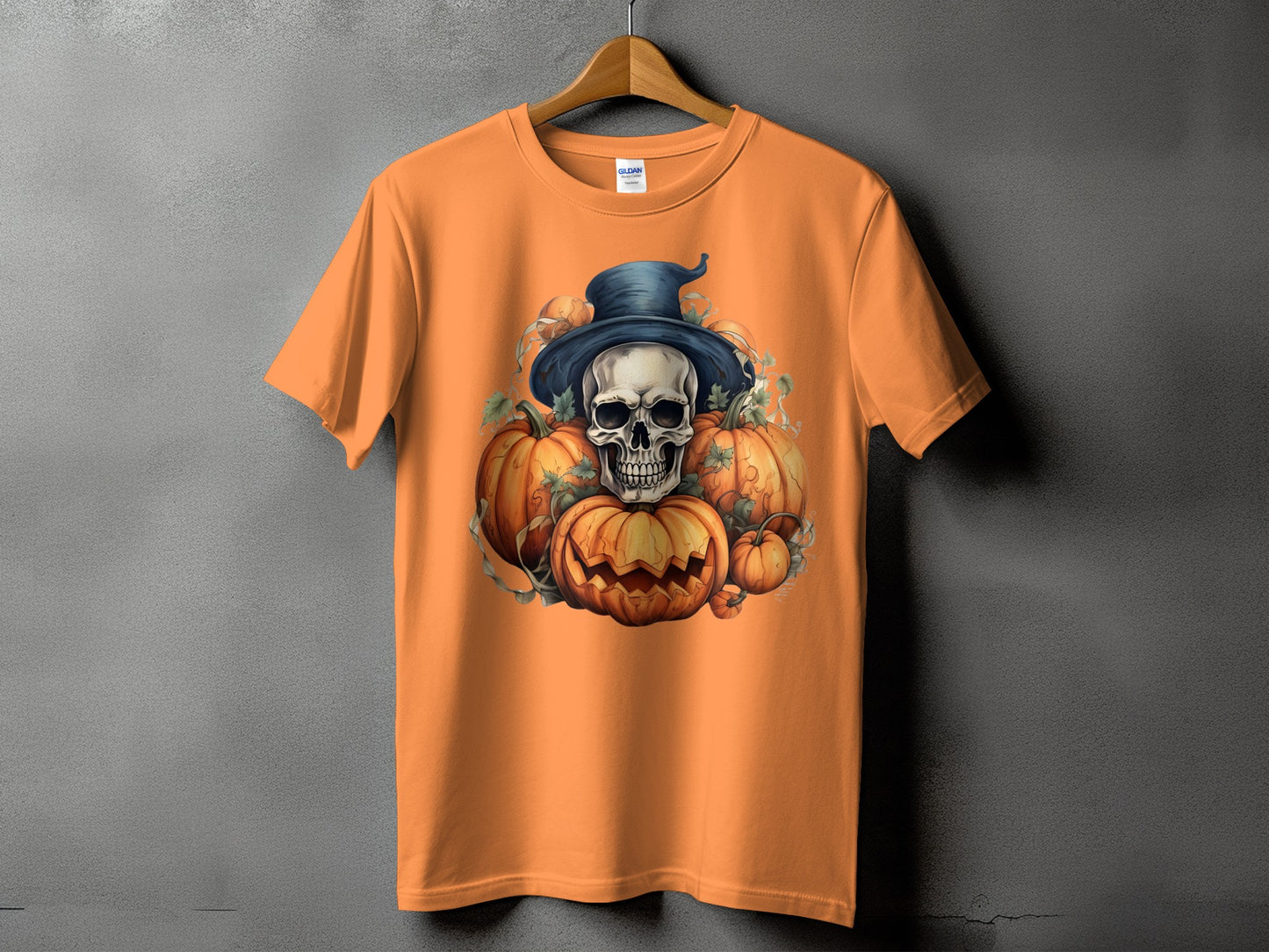 Orange t-shirt with Halloween skull and pumpkins graphic on gray background.