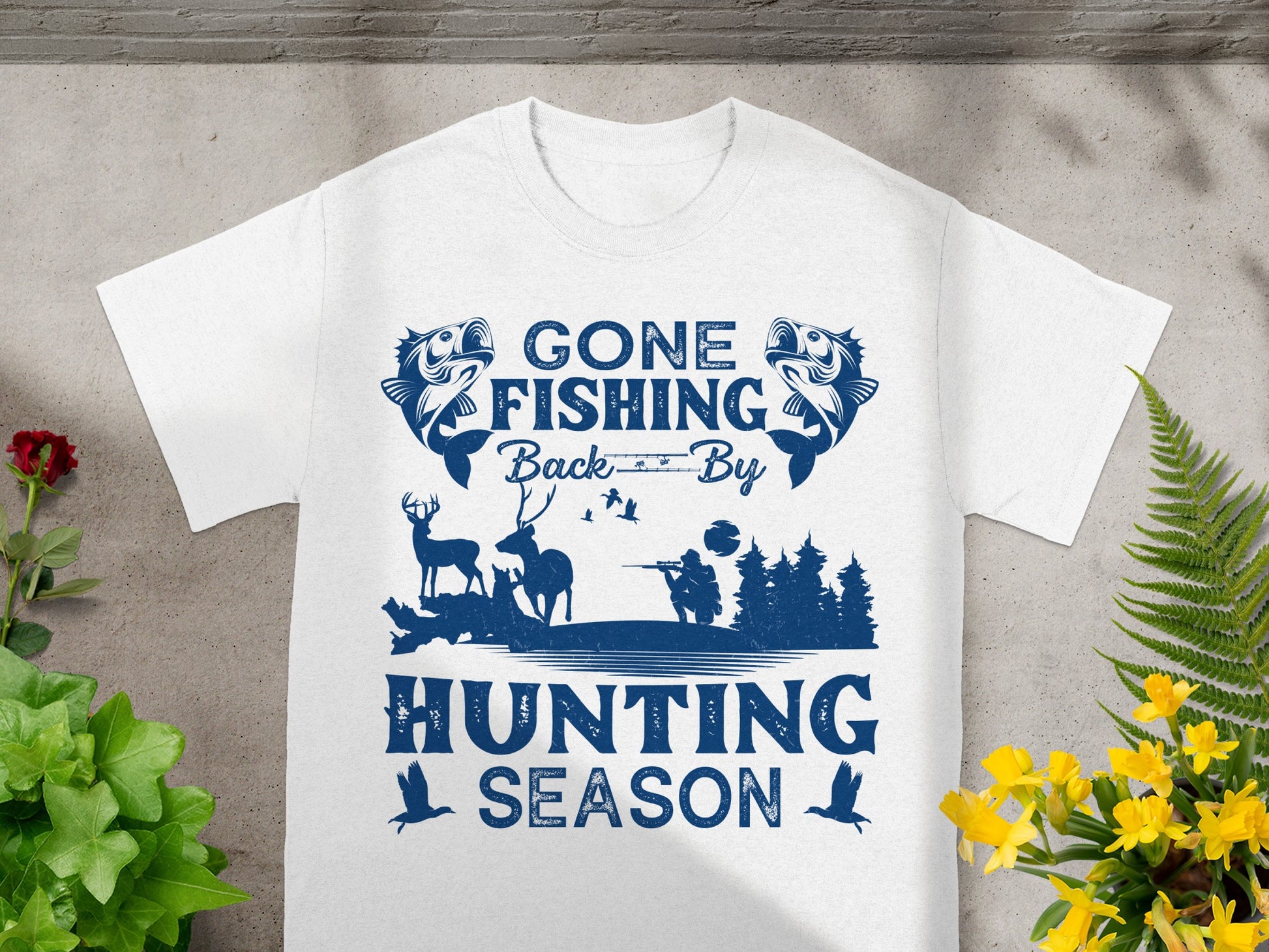 White t-shirt with blue graphic: "GONE FISHING Back By HUNTING SEASON", featuring fish, deer, hunter and trees.