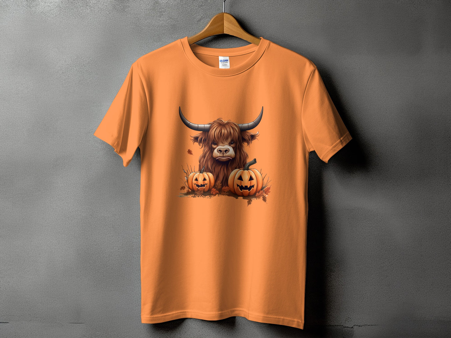 Orange t-shirt with a Highland cow and two jack-o'-lanterns graphic.