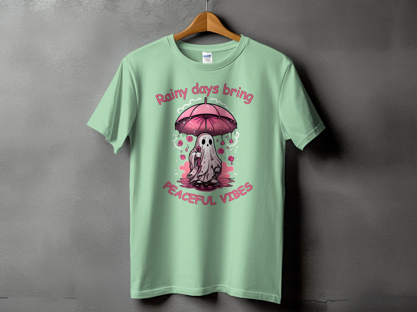 Light green t-shirt with ghost holding umbrella and text "Rainy days bring peaceful vibes."
