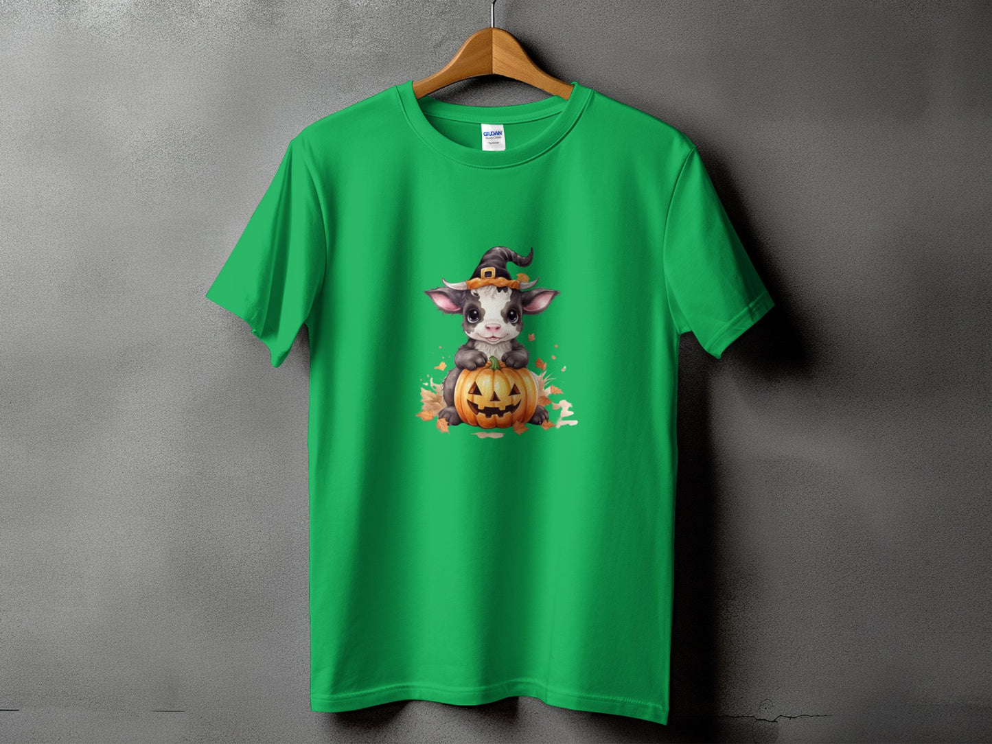Green t-shirt with cute cow wearing witch hat on pumpkin graphic.