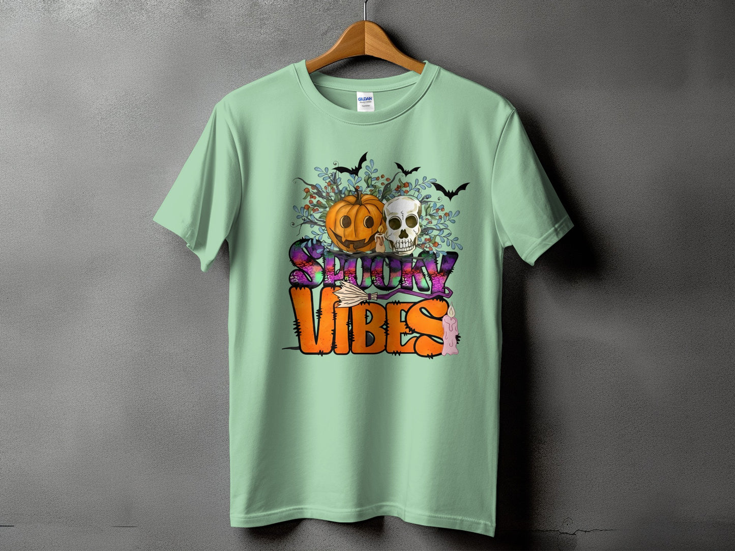 Light green t-shirt with a Halloween design featuring a pumpkin, skull, bats, and text.