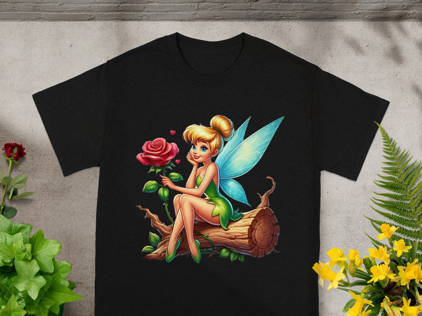 Tinkerbell fairy with a rose sits on a log, printed on a black t-shirt.