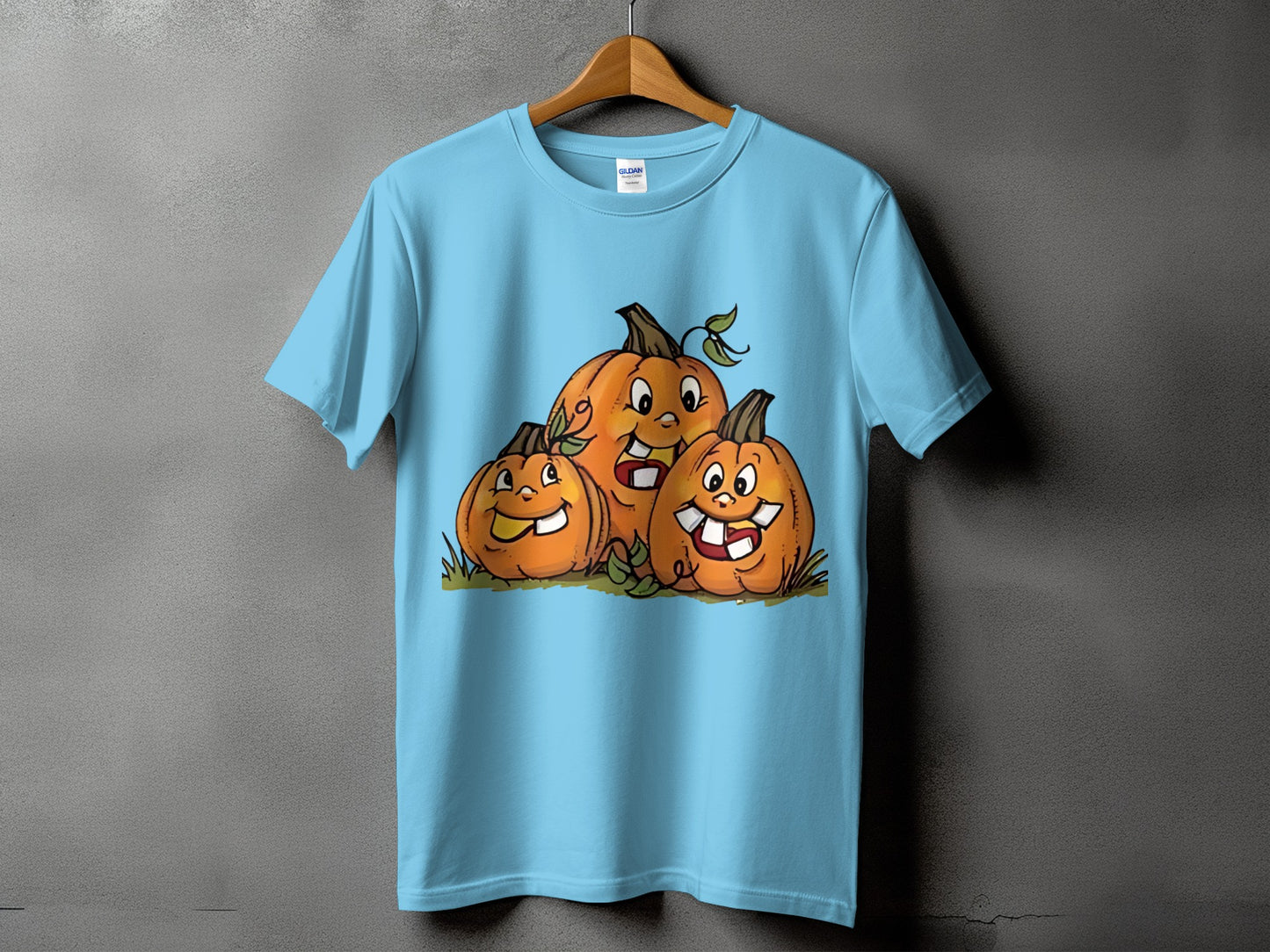 Light blue t-shirt with a graphic of three smiling cartoon pumpkins.
