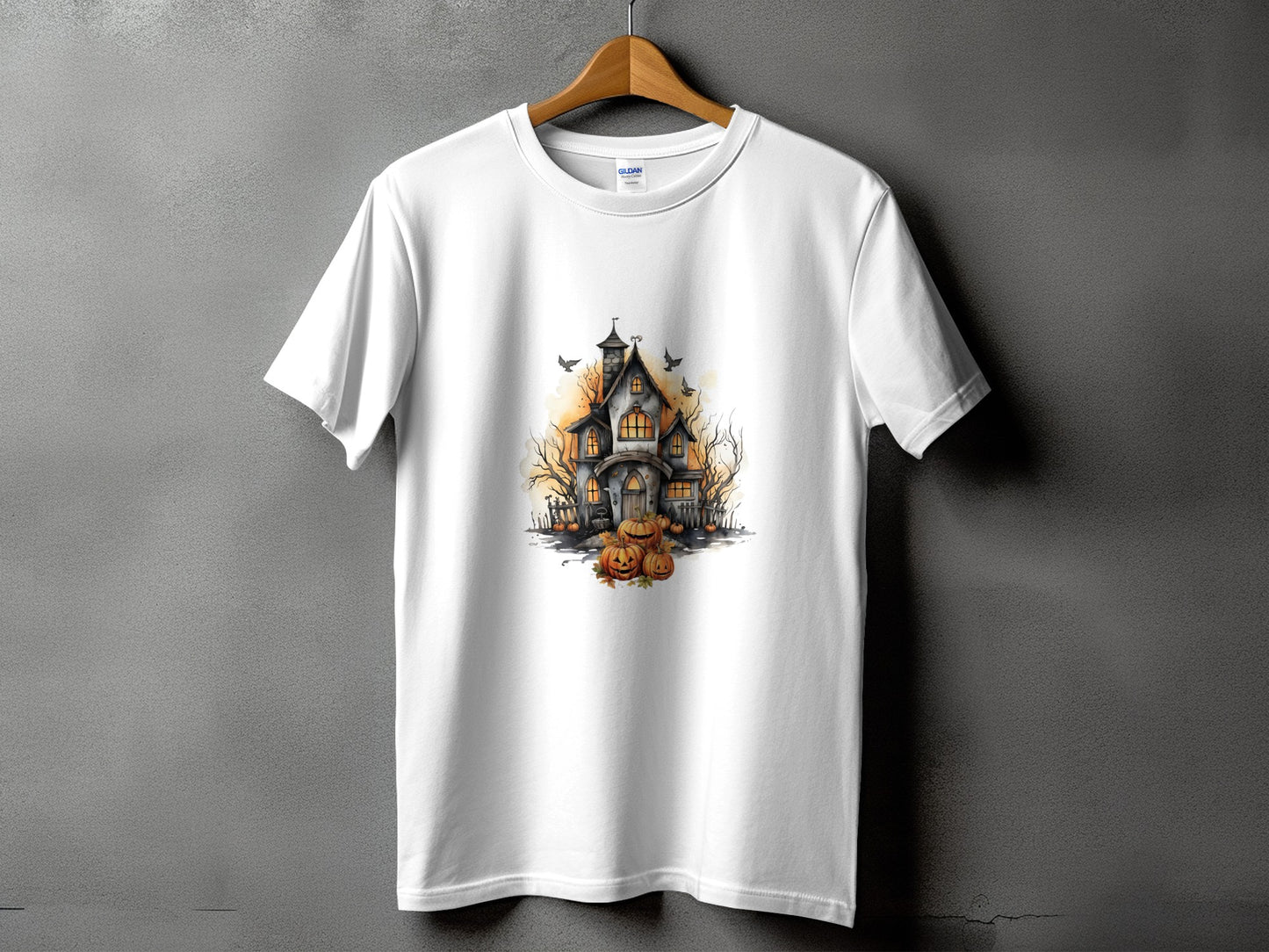 White t-shirt with a watercolor design of a spooky haunted house and pumpkins.