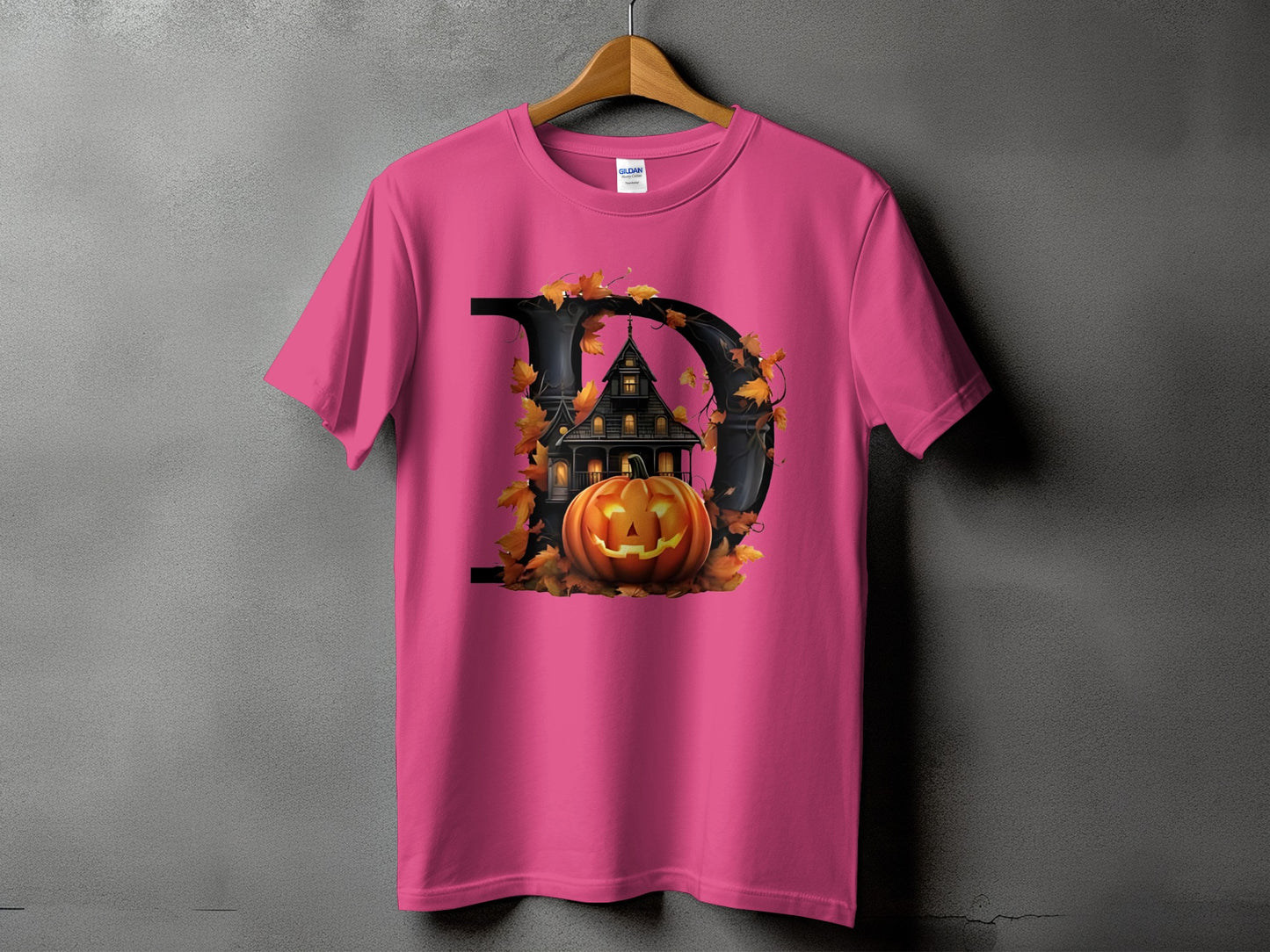 Pink t-shirt with black letter D featuring haunted house, jack-o-lantern, and autumn leaves.