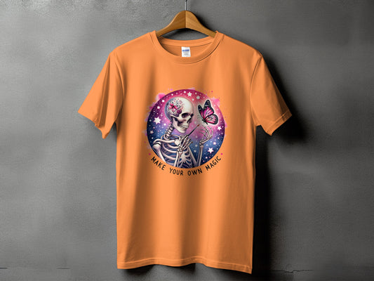 Orange t-shirt with skeleton painting a butterfly with the words "Make Your Own Magic".