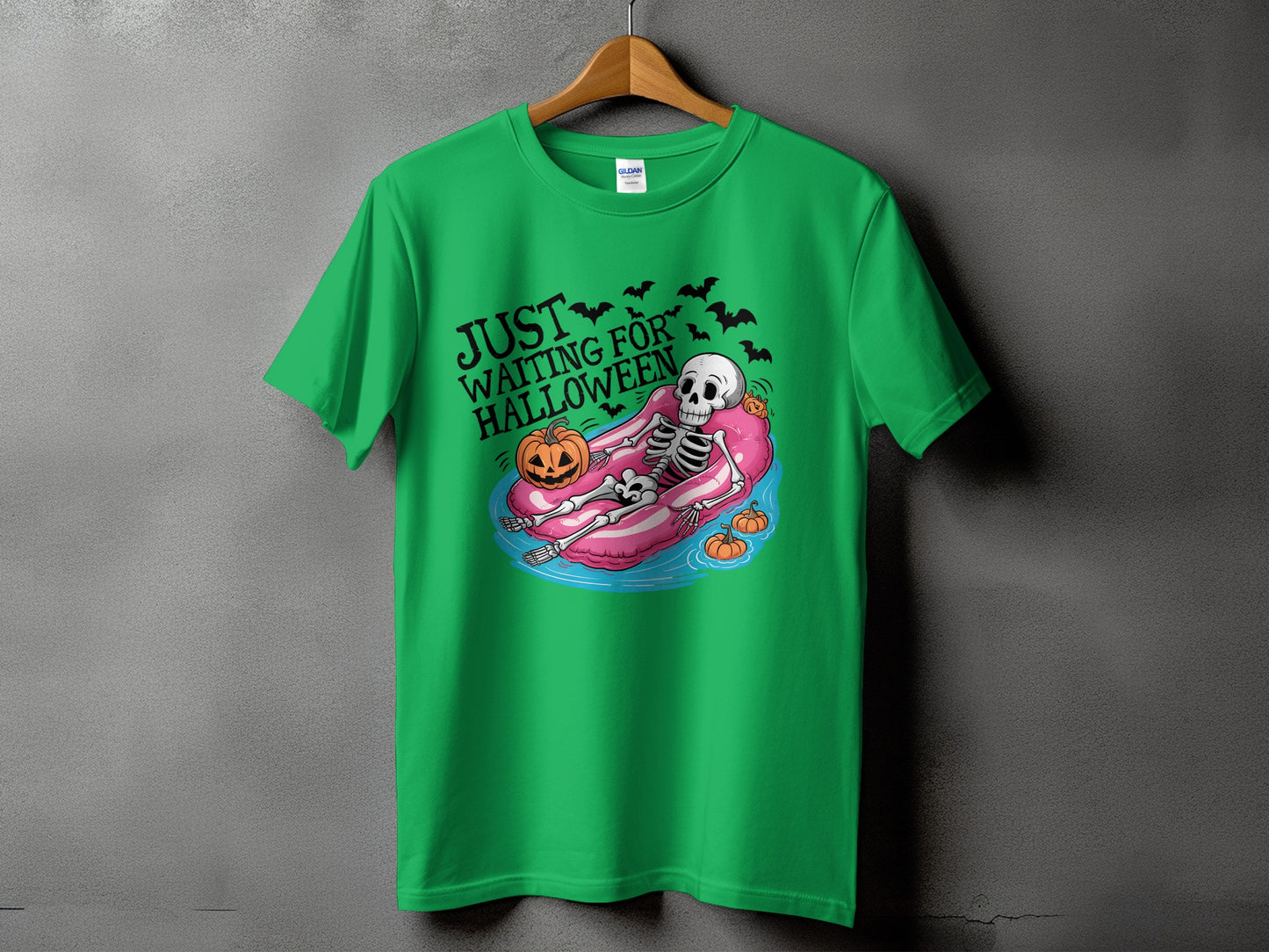 Green t-shirt with skeleton floating on pink tube and text "JUST WAITING FOR HALLOWEEN".