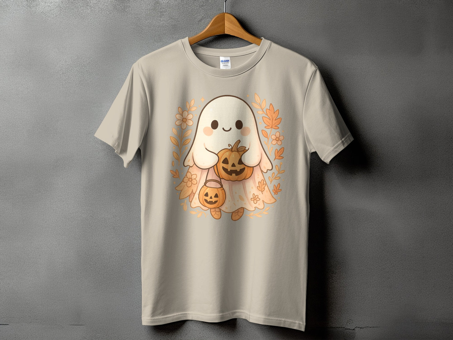 Cute ghost holding pumpkins surrounded by leaves and flowers on a tan t-shirt.