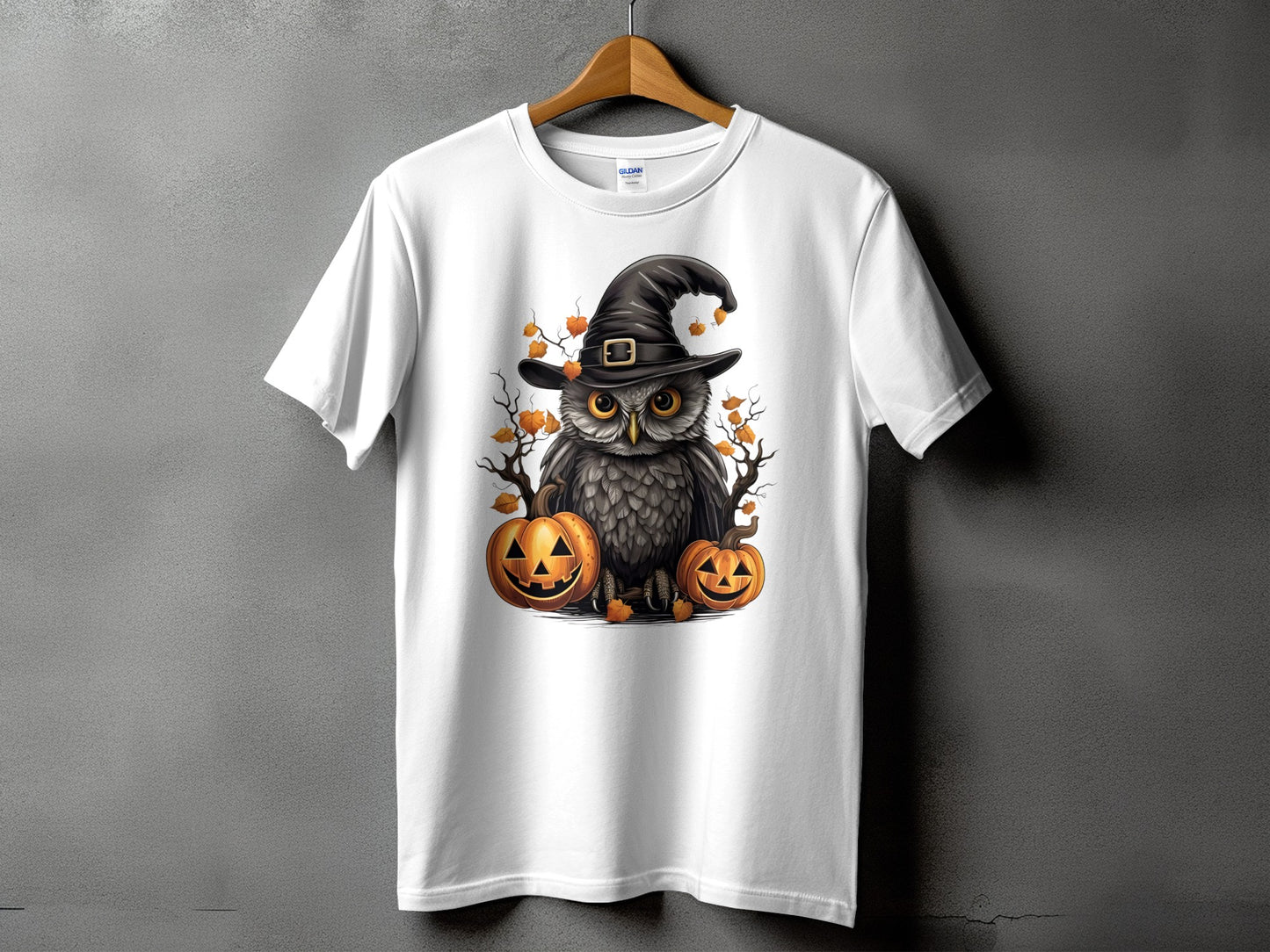 White t-shirt with an owl wearing a witch hat surrounded by pumpkins and autumn leaves.