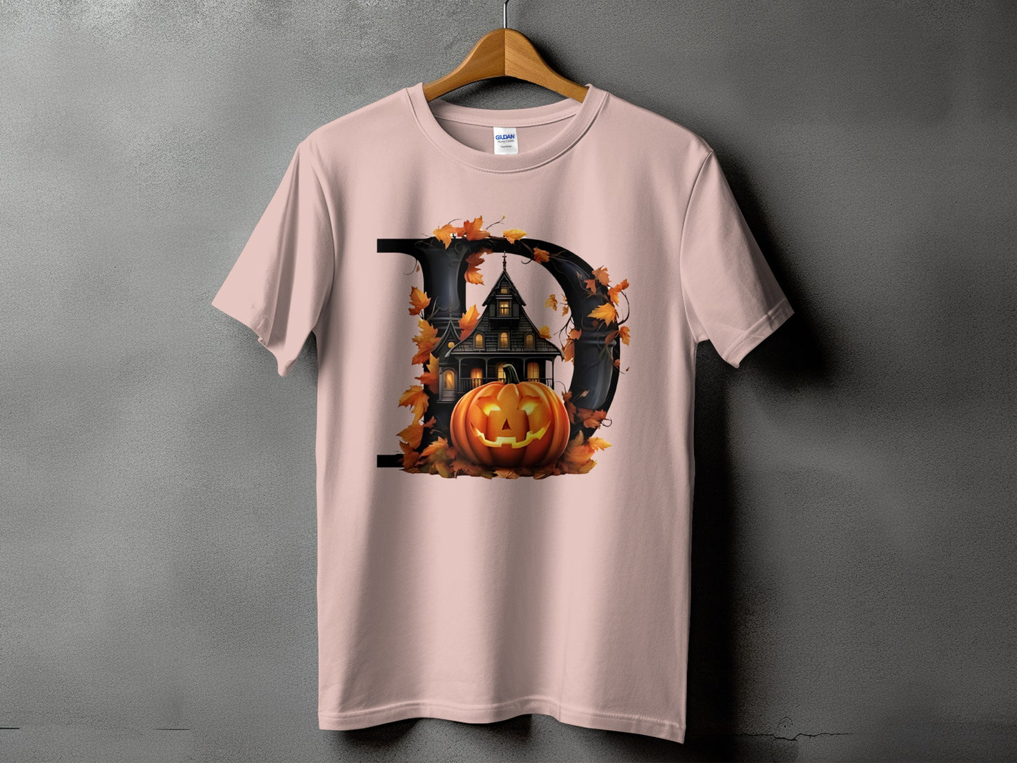 Pink t-shirt with a large black letter D, haunted house, pumpkin, and autumn leaves.